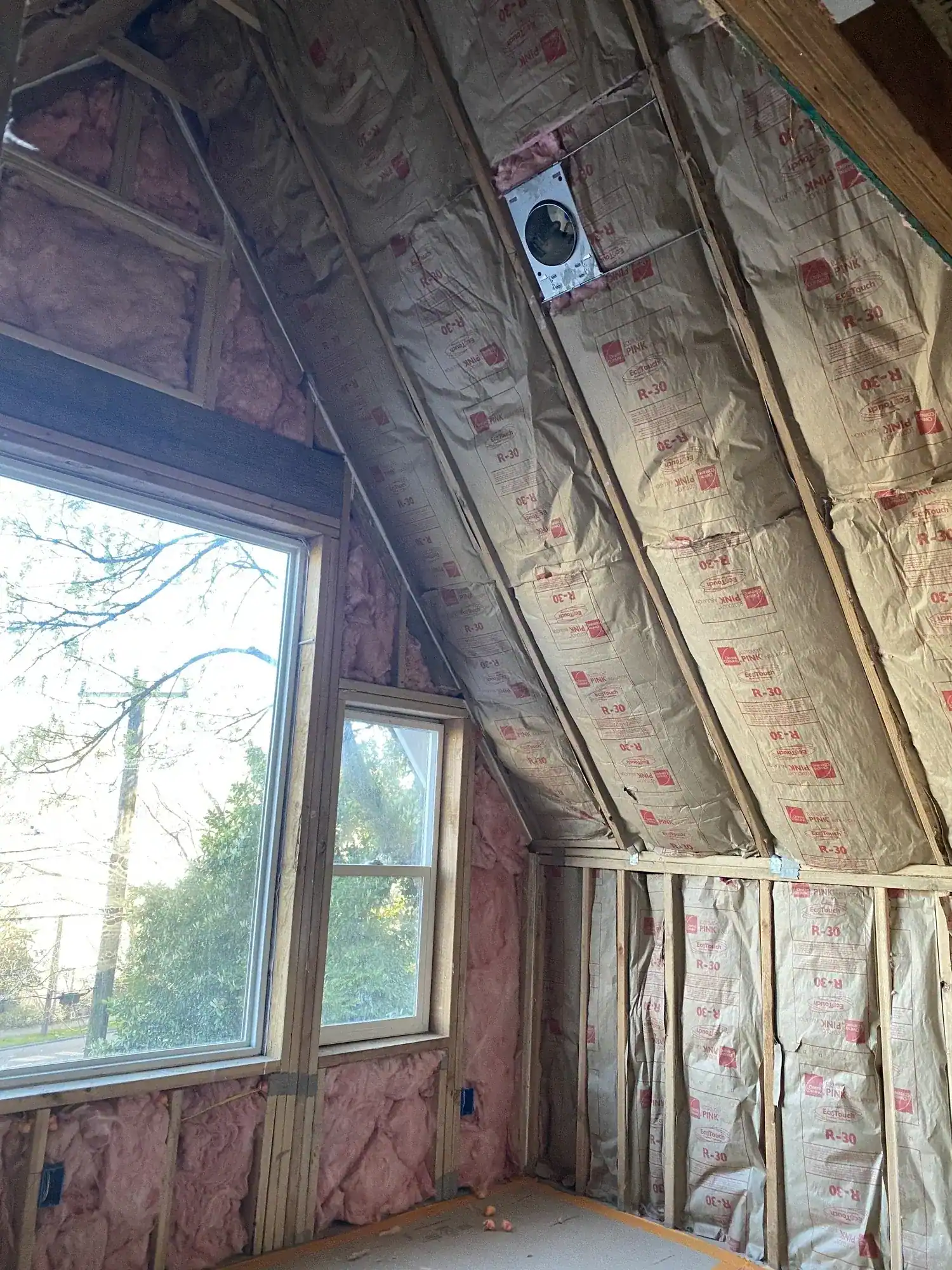 Pink batt insulation installed in the sloped upper-floor walls around a window