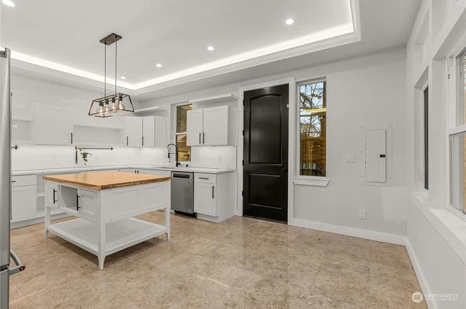 Kitchen with a butcher-block island, white cabinets, a pendant light, and a black door
