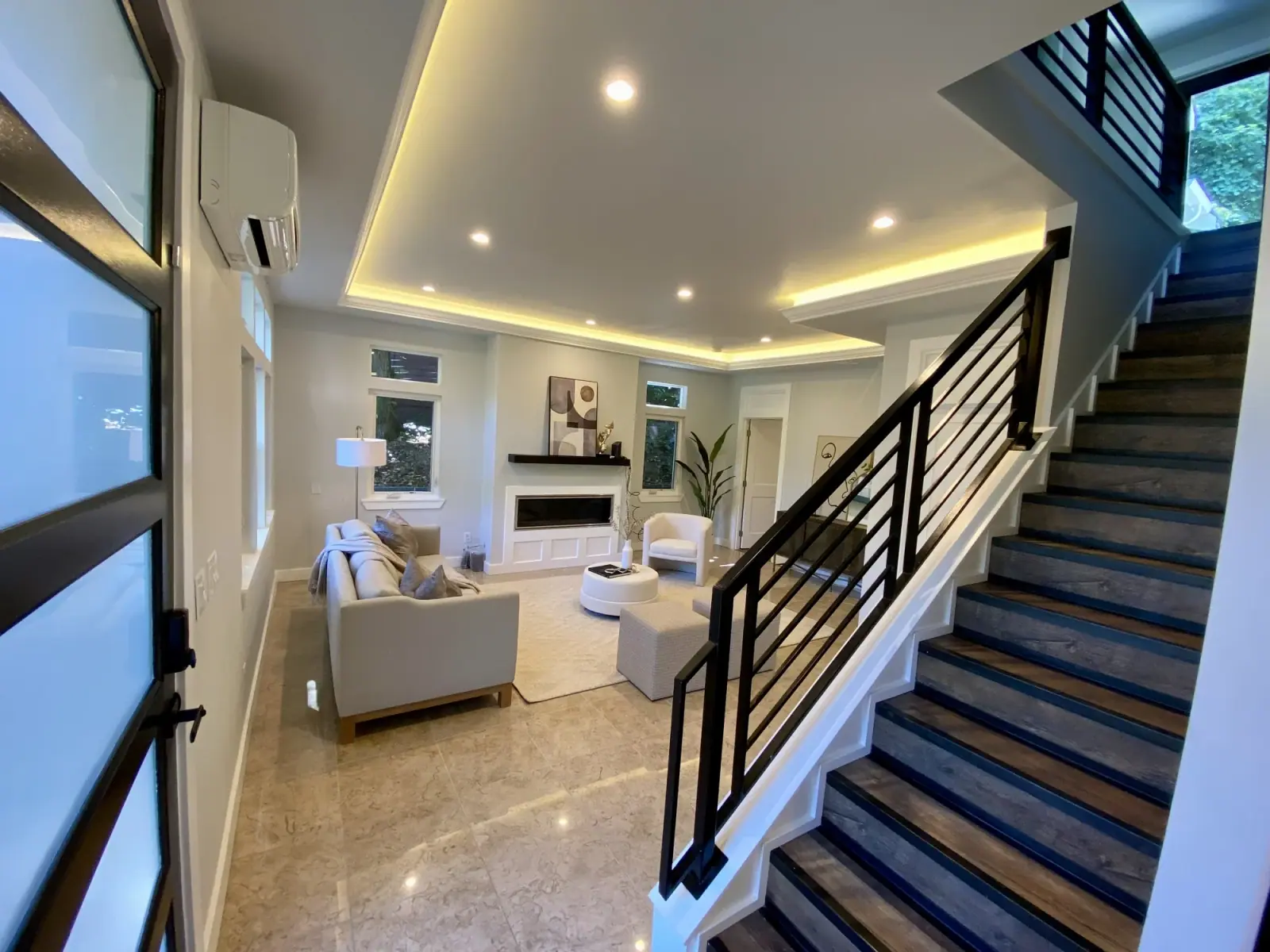 Finished living room with a fireplace, black-railed stair, and LED-lit tray ceiling