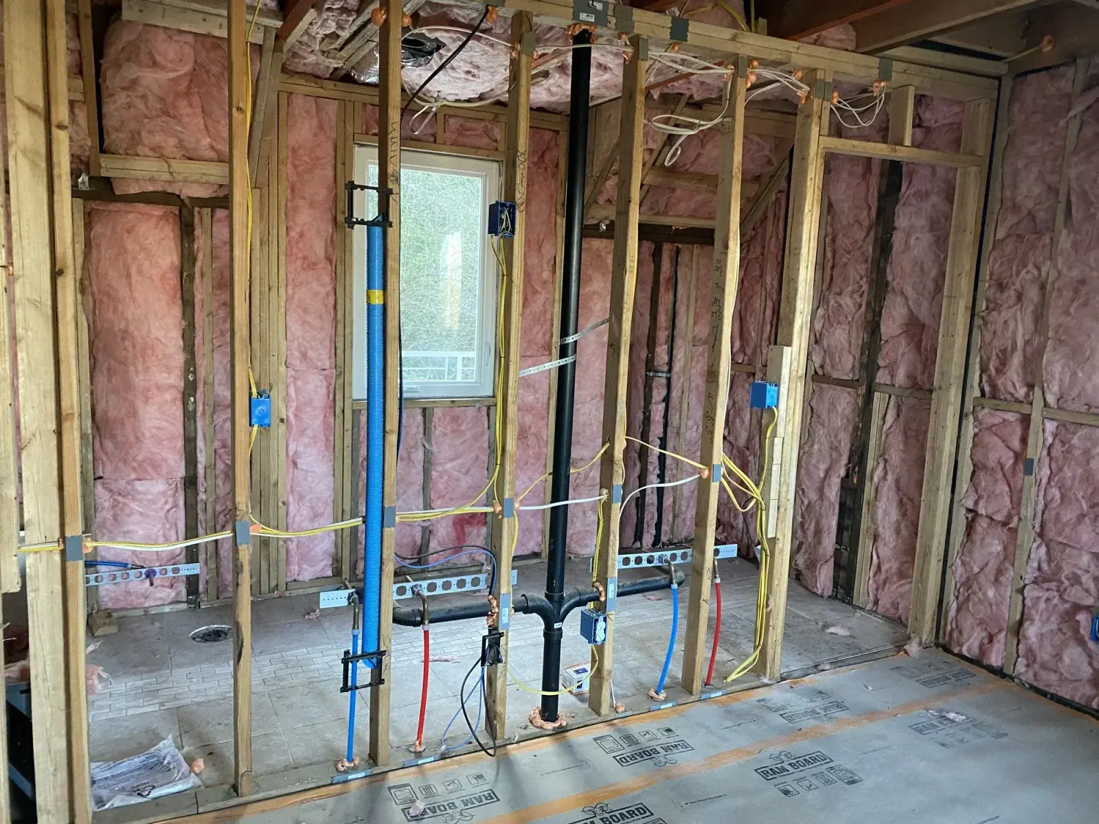 Red and blue PEX supply lines and pink batt insulation in a framed bathroom wall