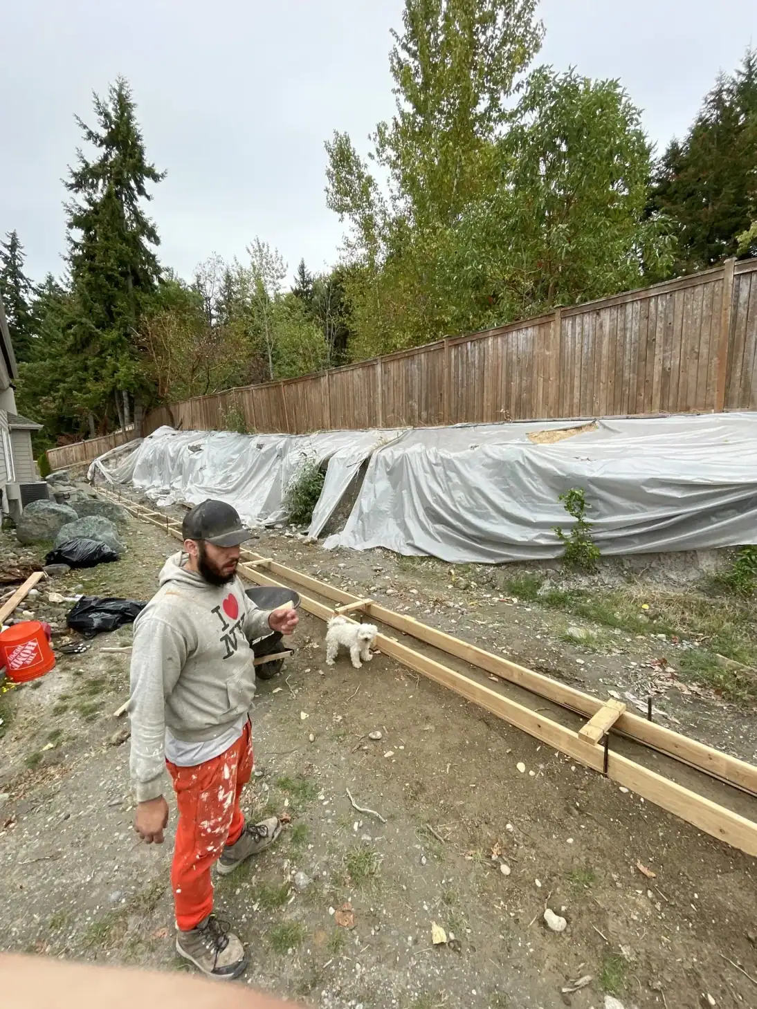 Crew member beside the long footing form in a Bellevue side yard, with the cut slope covered in white membrane
