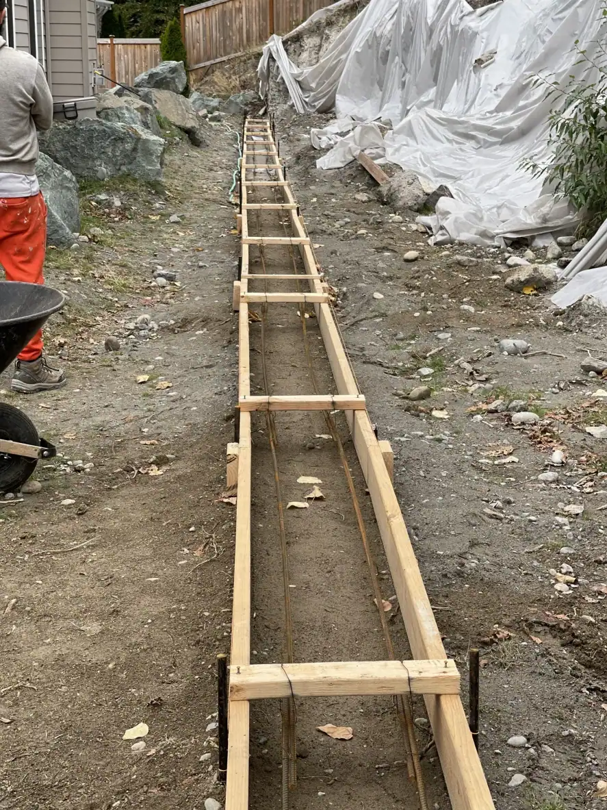 Looking down the wooden footing form with rebar along the plastic-covered slope