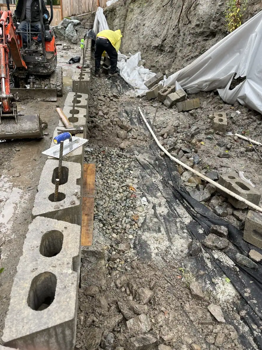 Mini excavator and crew laying the first CMU block courses on the cured footing