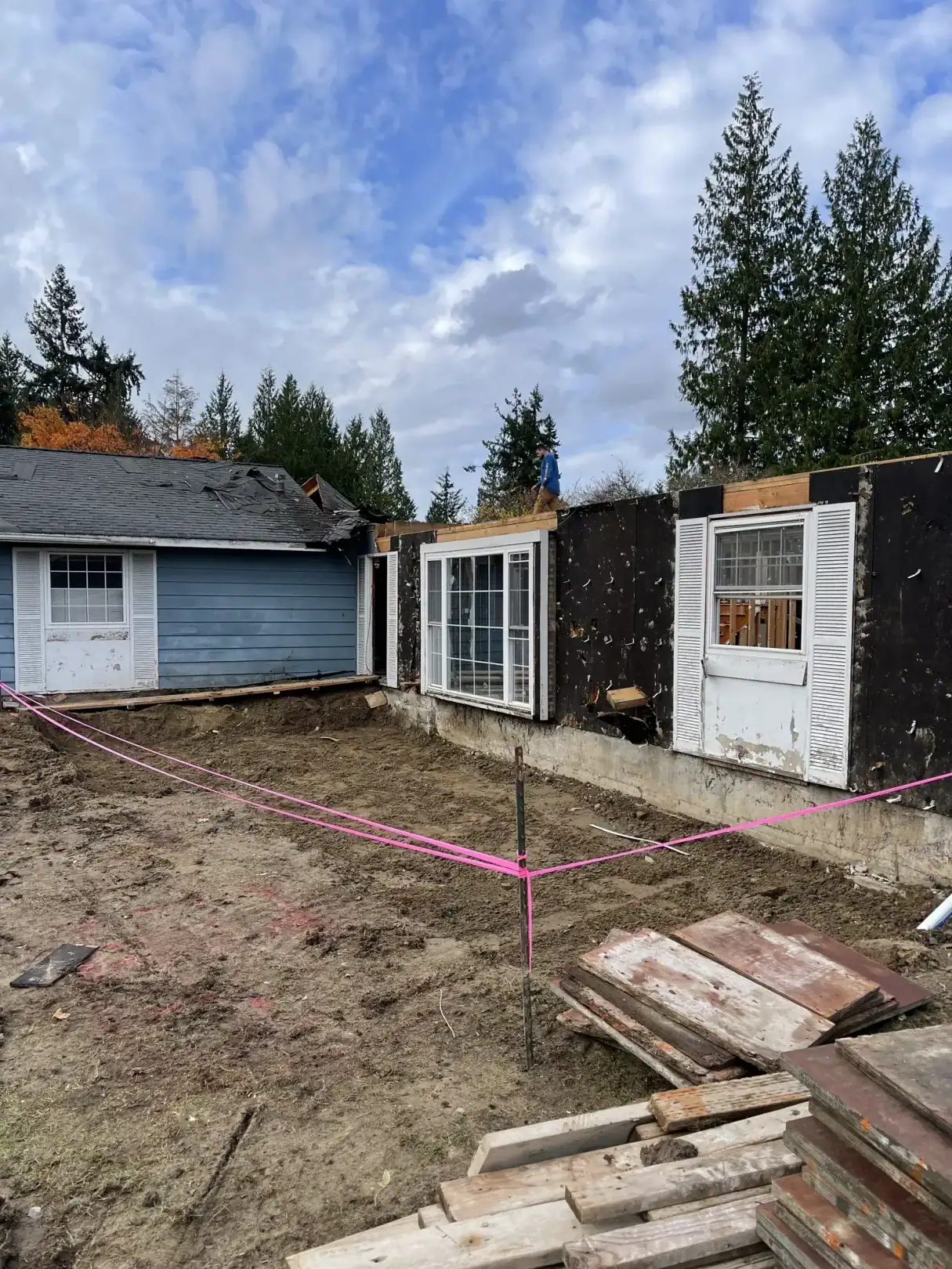 Cleared Bellevue lot with pink layout string, a lumber stack, and the old shed before the new foundation
