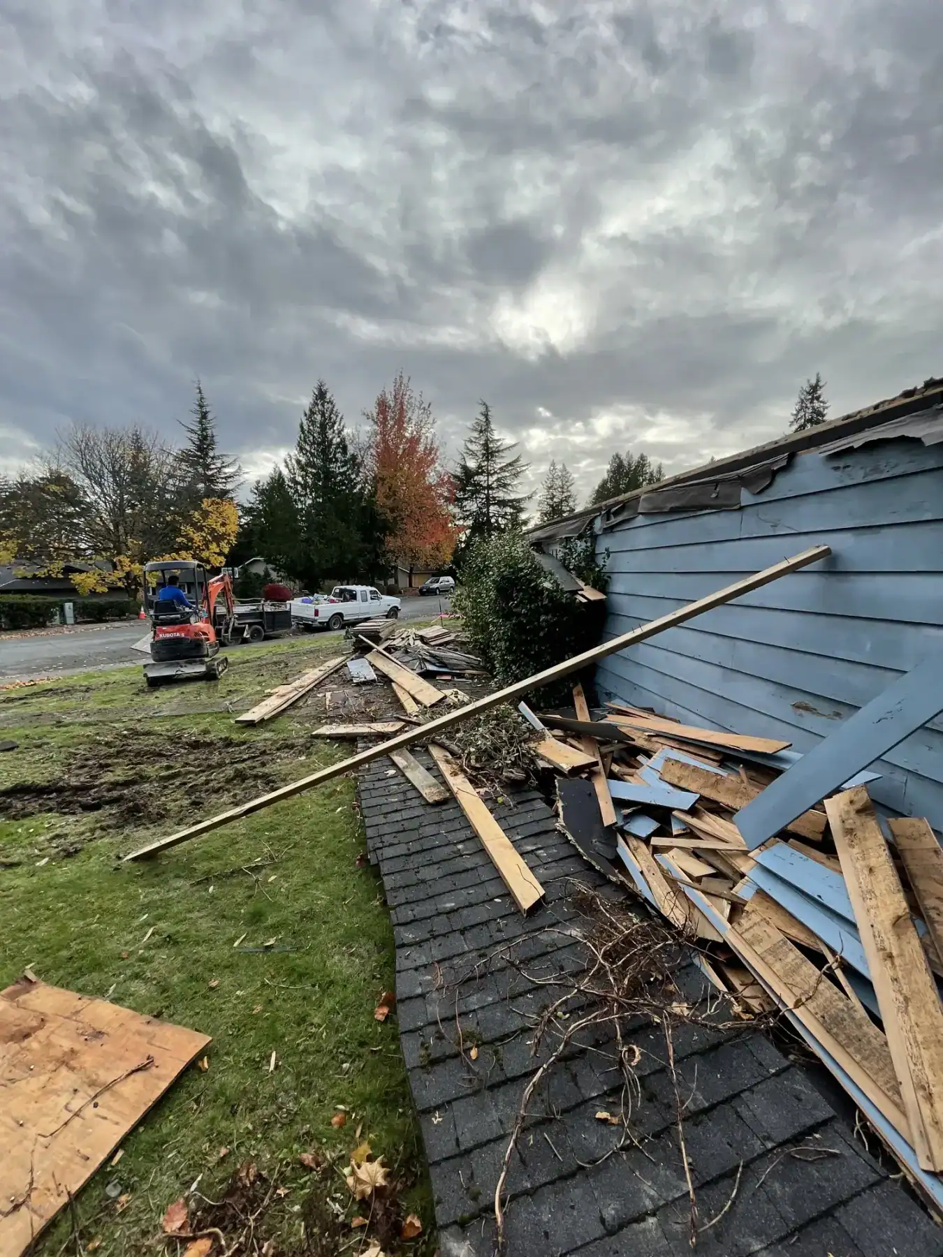 Torn-off roofing and lumber beside the old house, viewed from the street