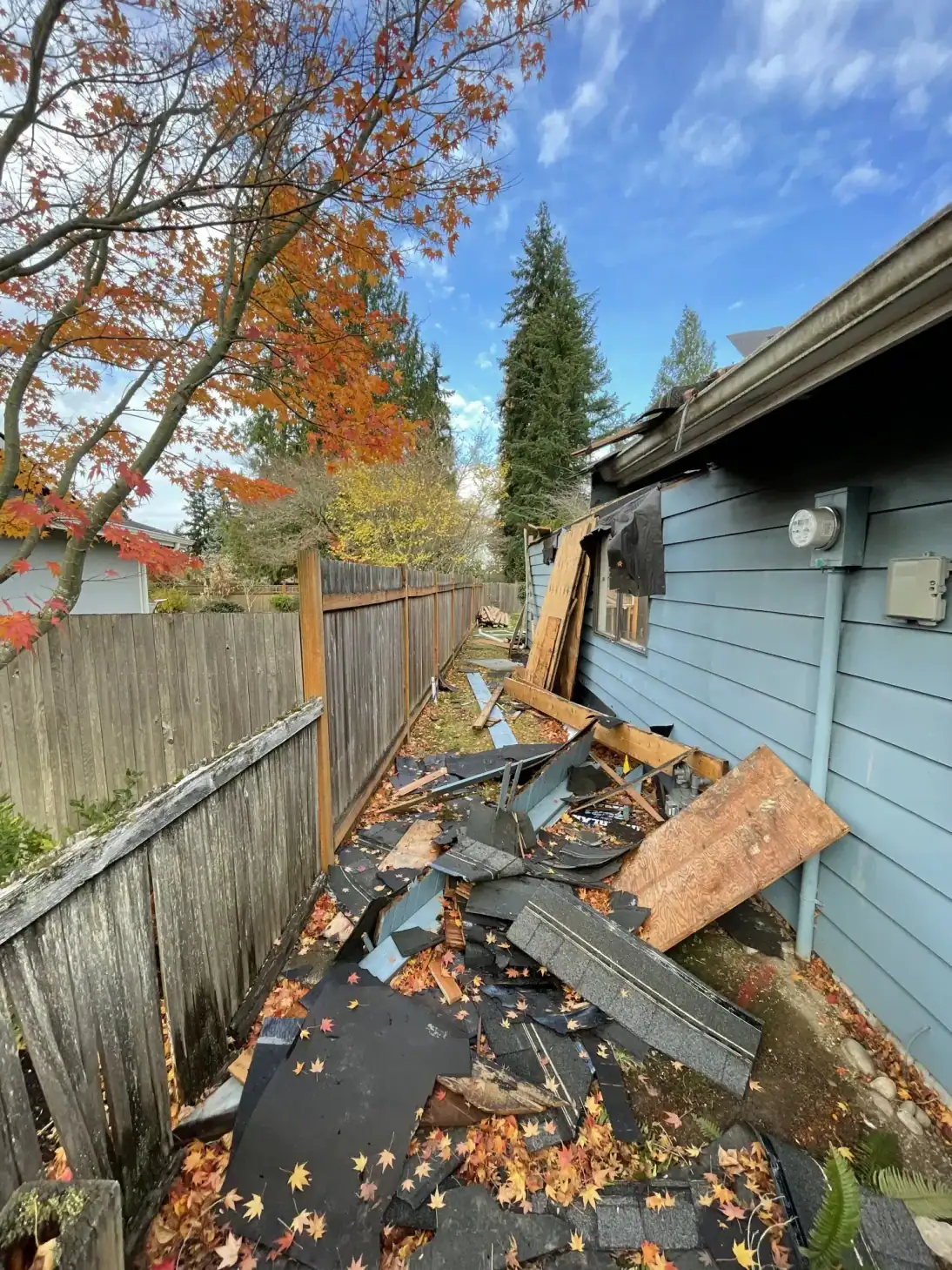 Side yard of the old house with fence, fallen leaves, and demolition debris