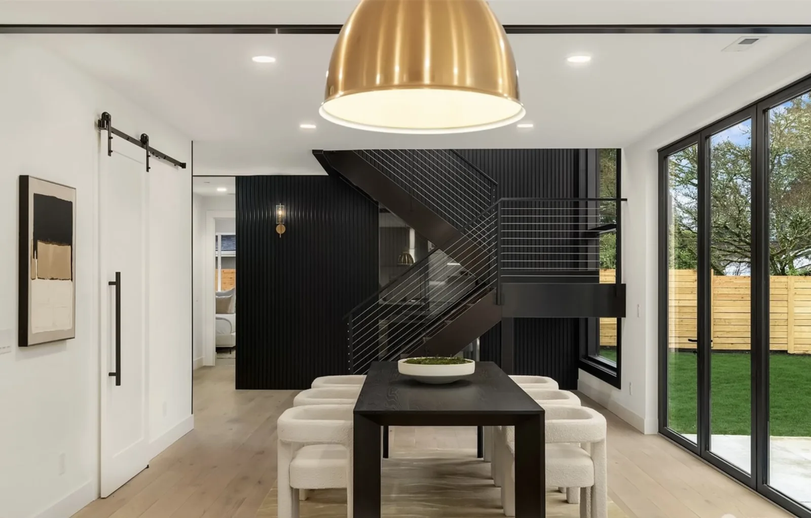 Dining room under a brass pendant with the black-slat stair wall and sliding doors to the backyard