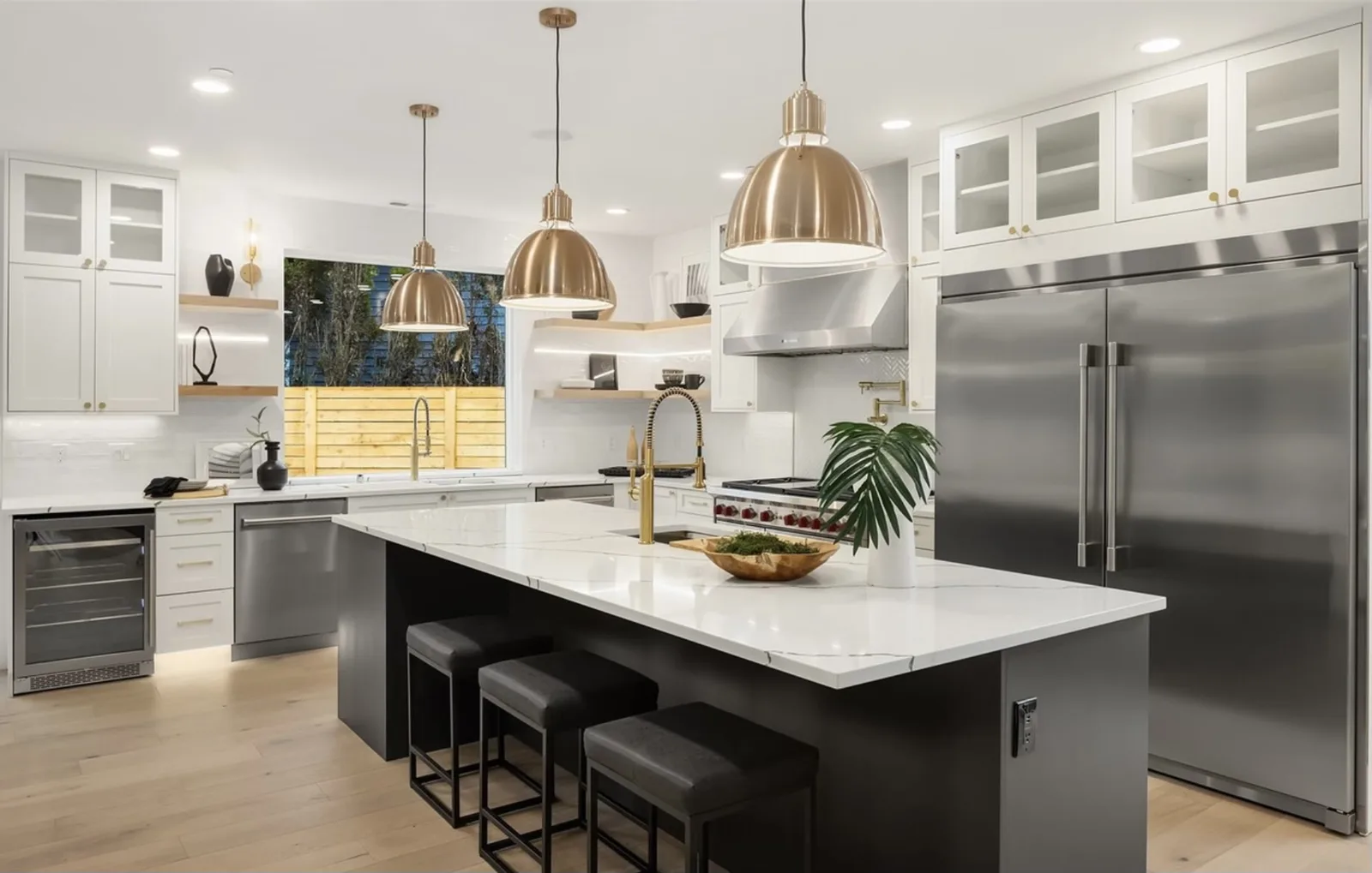 Straight-on kitchen view: black island with white quartz, green tile backsplash, brass pendants, and a stainless hood