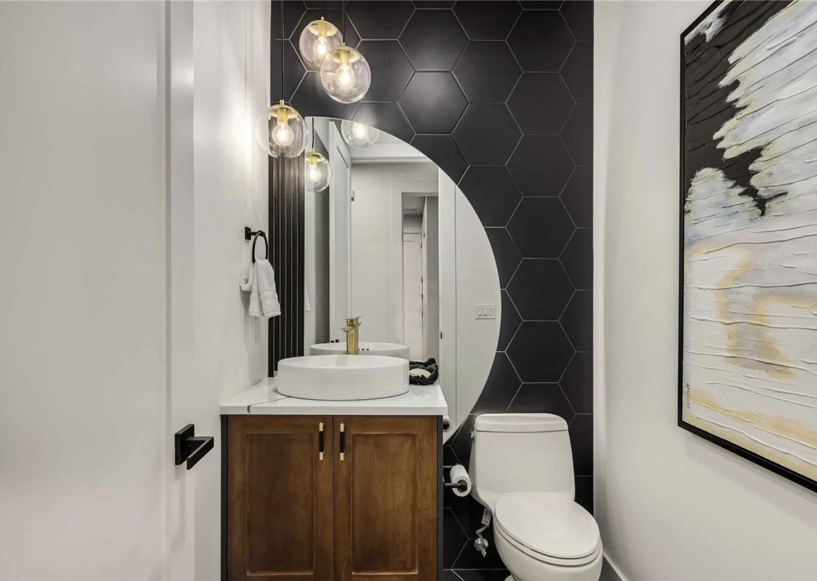 Second view of the powder room's black hex tile, vessel sink, and brass lighting