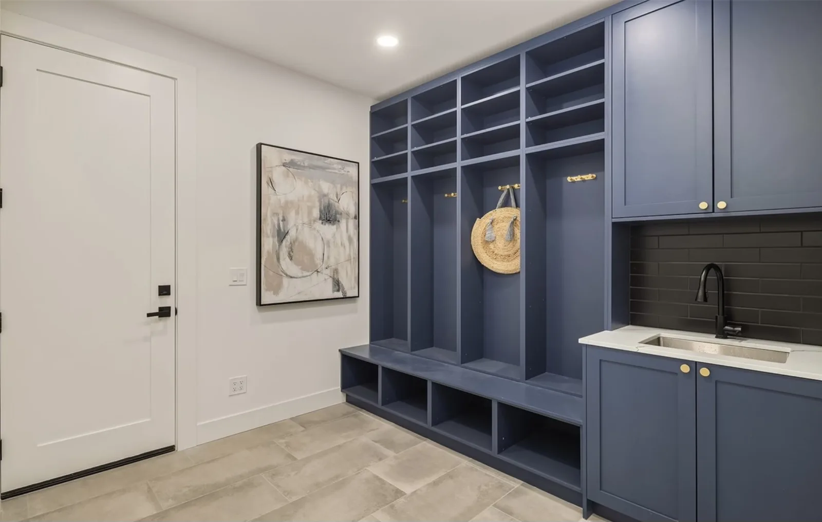Mudroom with navy built-in lockers and cubbies and a utility sink with black tile backsplash
