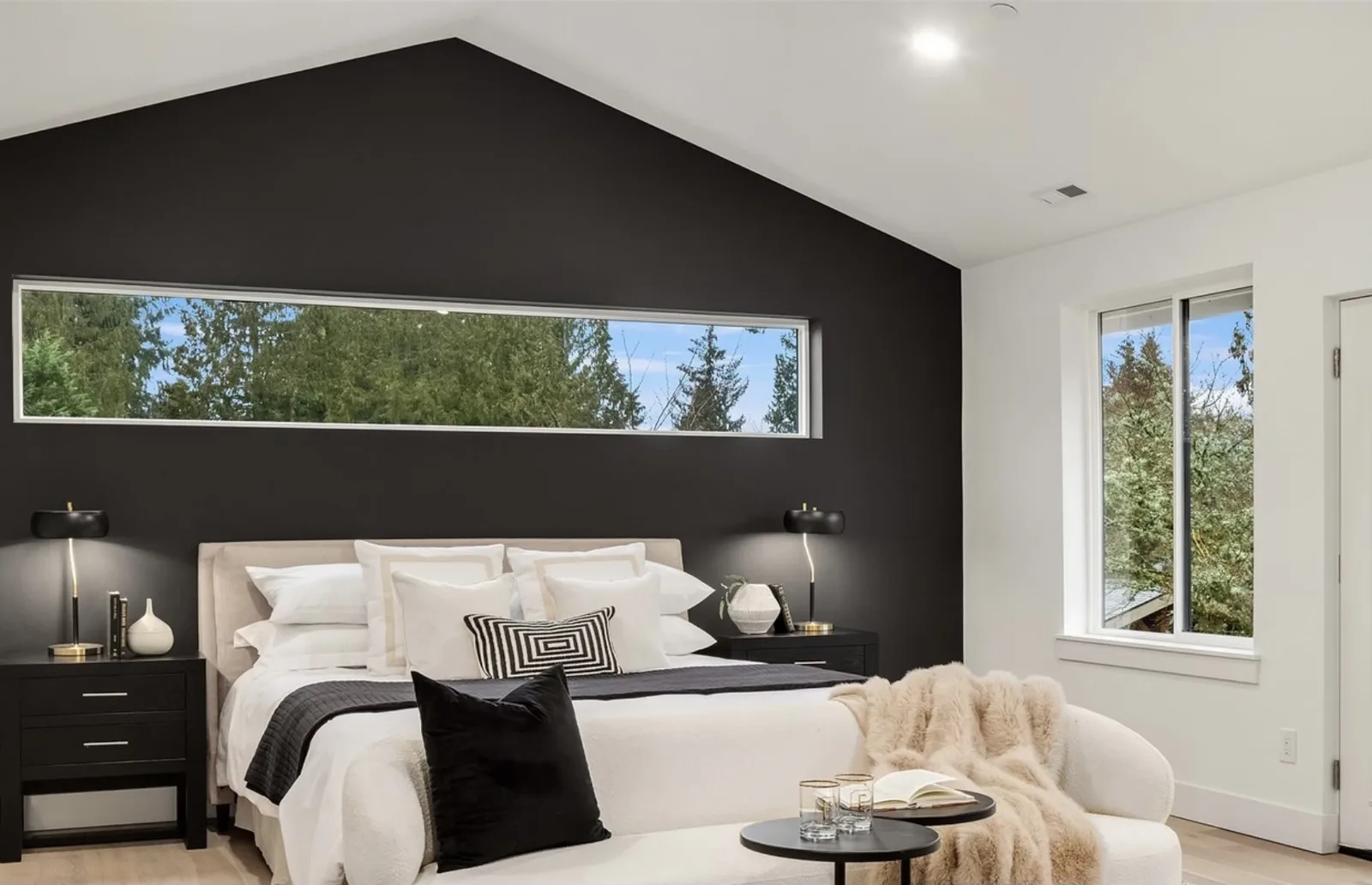 Primary bedroom with a vaulted ceiling, black accent wall, and a long clerestory window above the bed