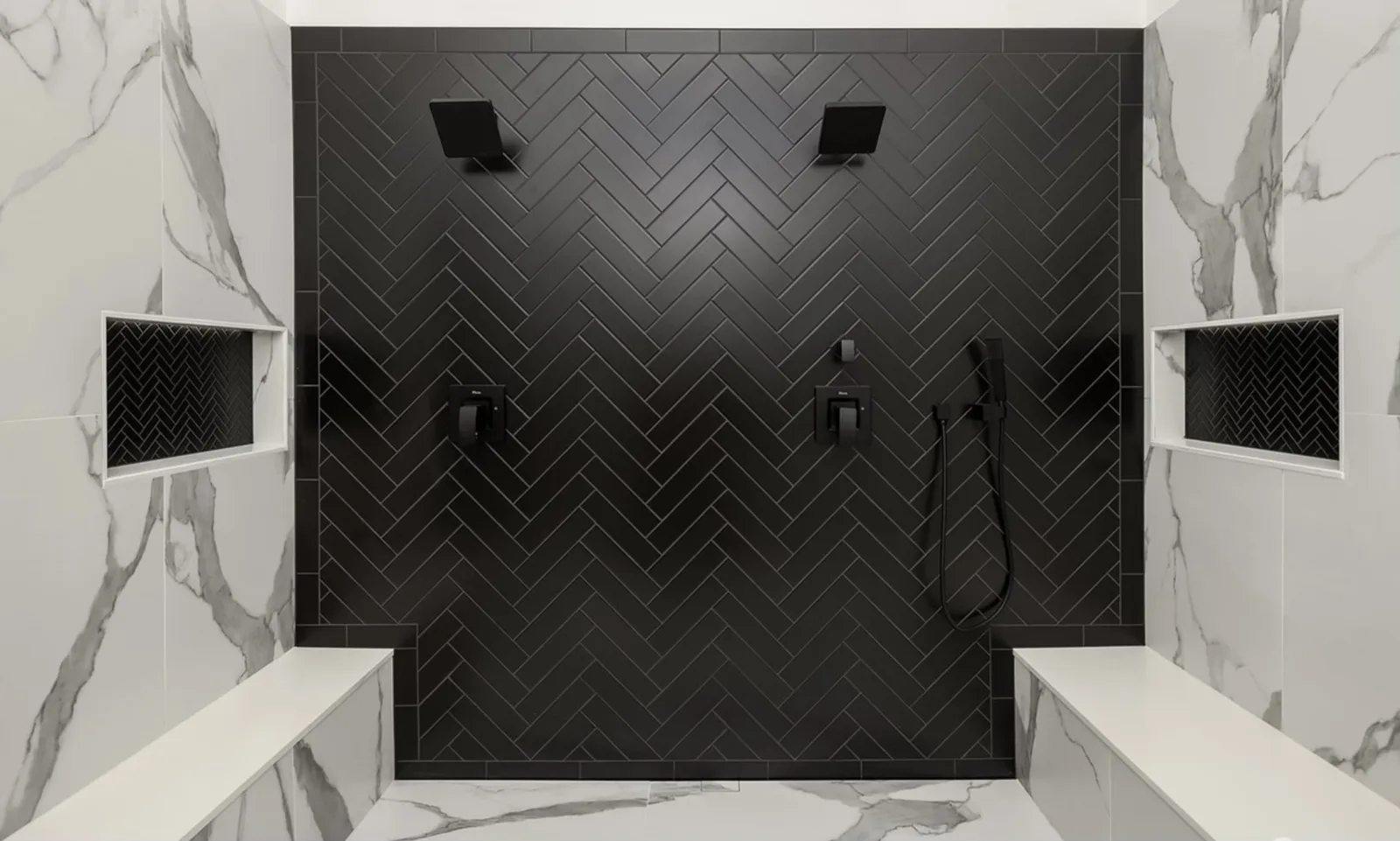 Black herringbone tile double shower with two shower heads inside the marble primary bath