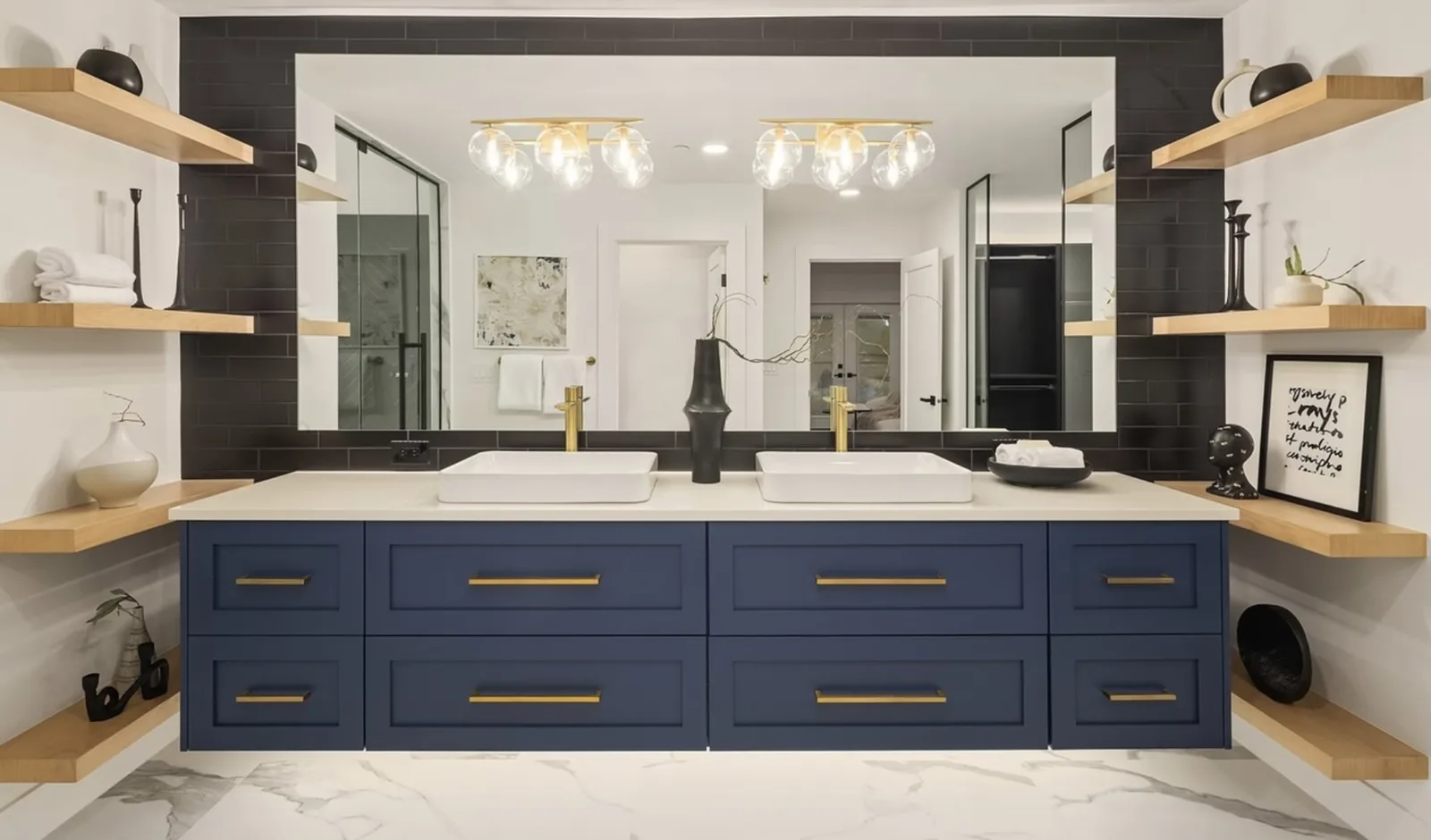 Navy double vanity with brass pulls, floating oak shelves, and a glass-bulb chandelier in the primary bath