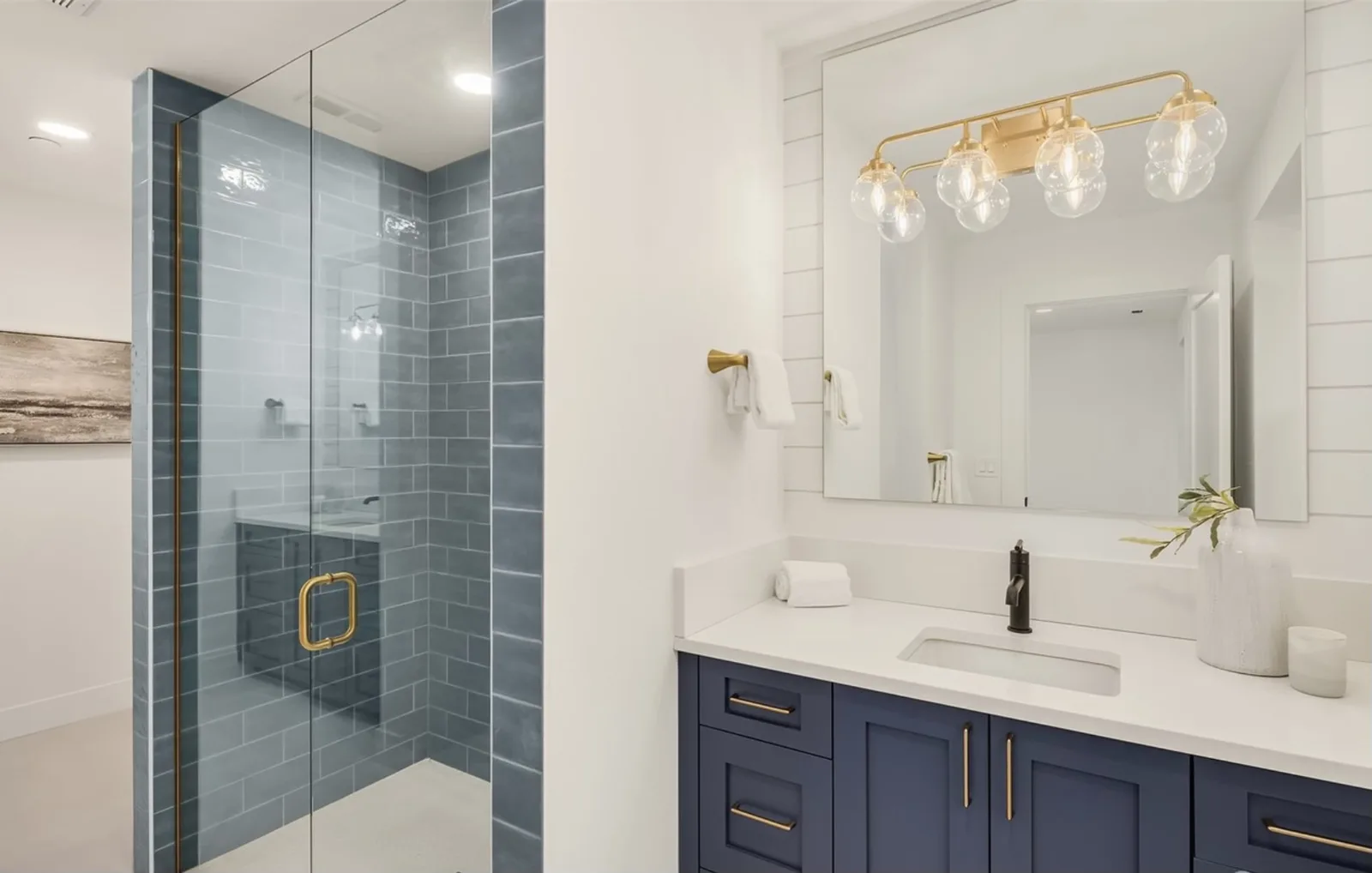 Guest bath with a blue tile shower, navy vanity, brass fixtures, and a glass-shade vanity light