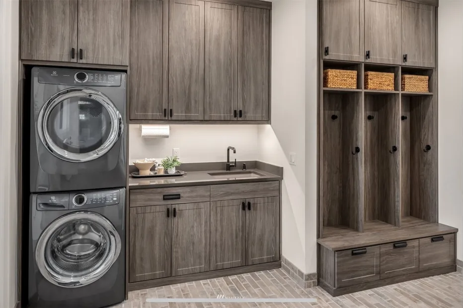 Laundry room with a stacked washer and dryer, gray-wood cabinetry, and mudroom bench cubbies