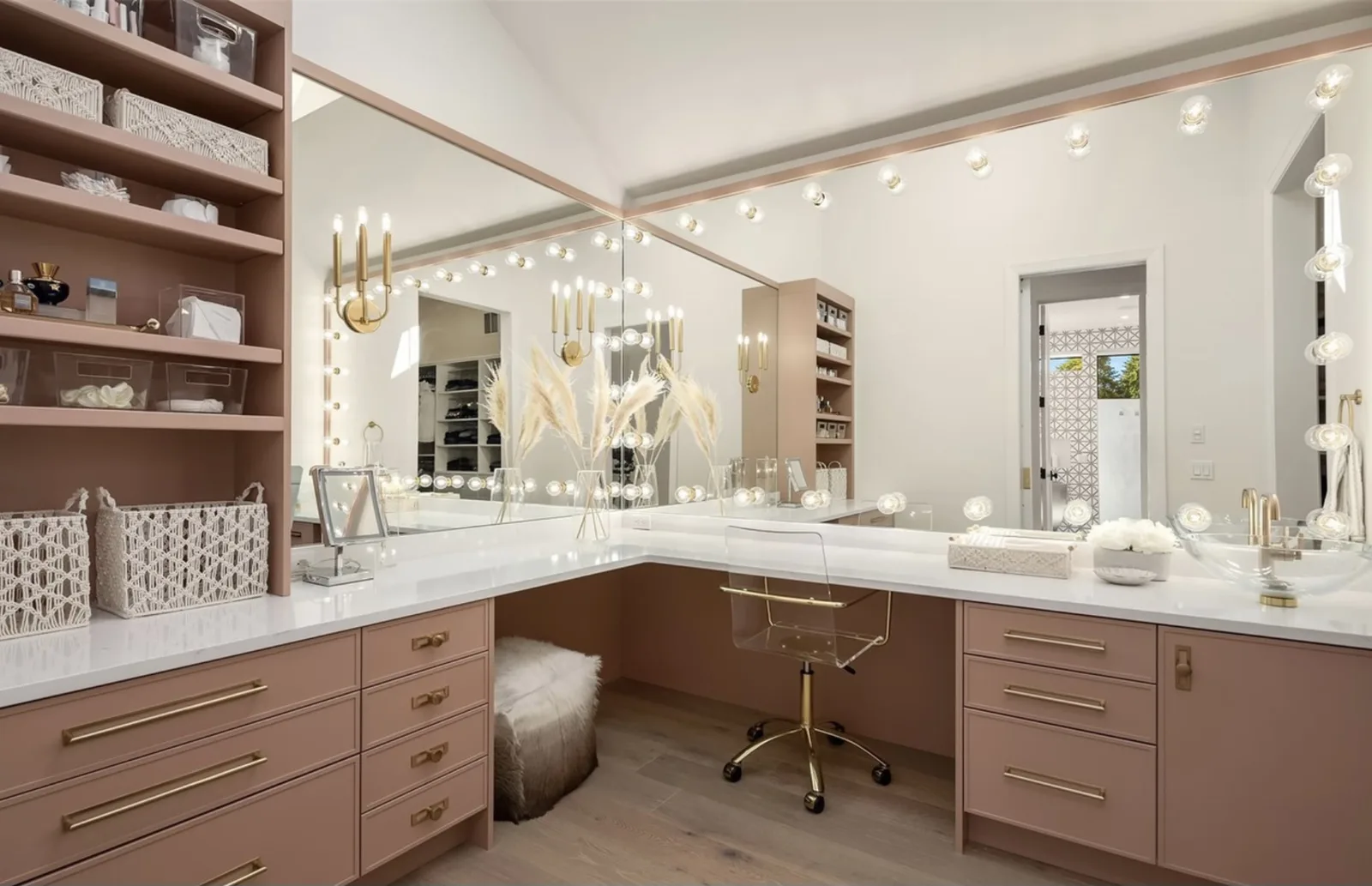 Hollywood-style makeup vanity room with lighted mirrors, blush-pink cabinetry, and open shelving