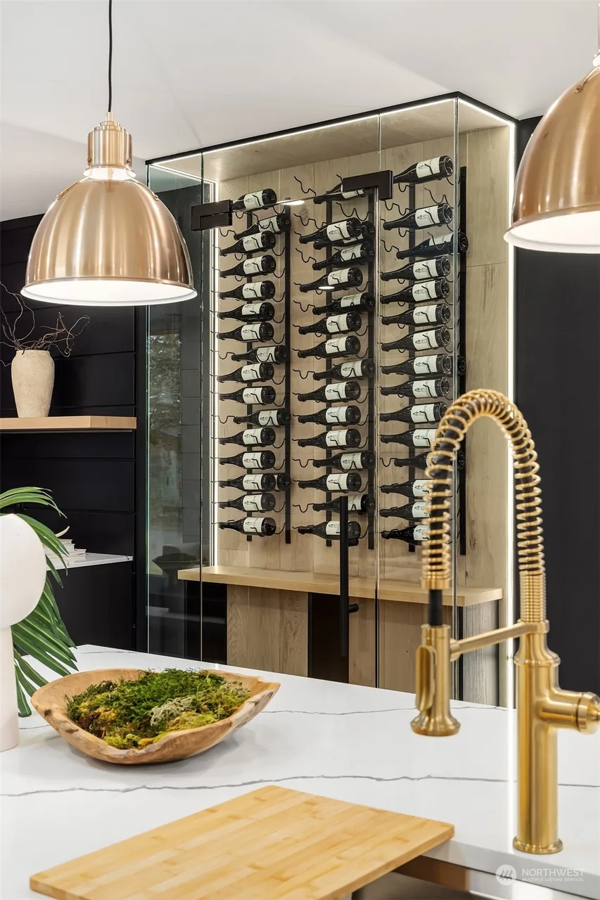 Brass gooseneck faucet at the kitchen island with the lit wine display behind