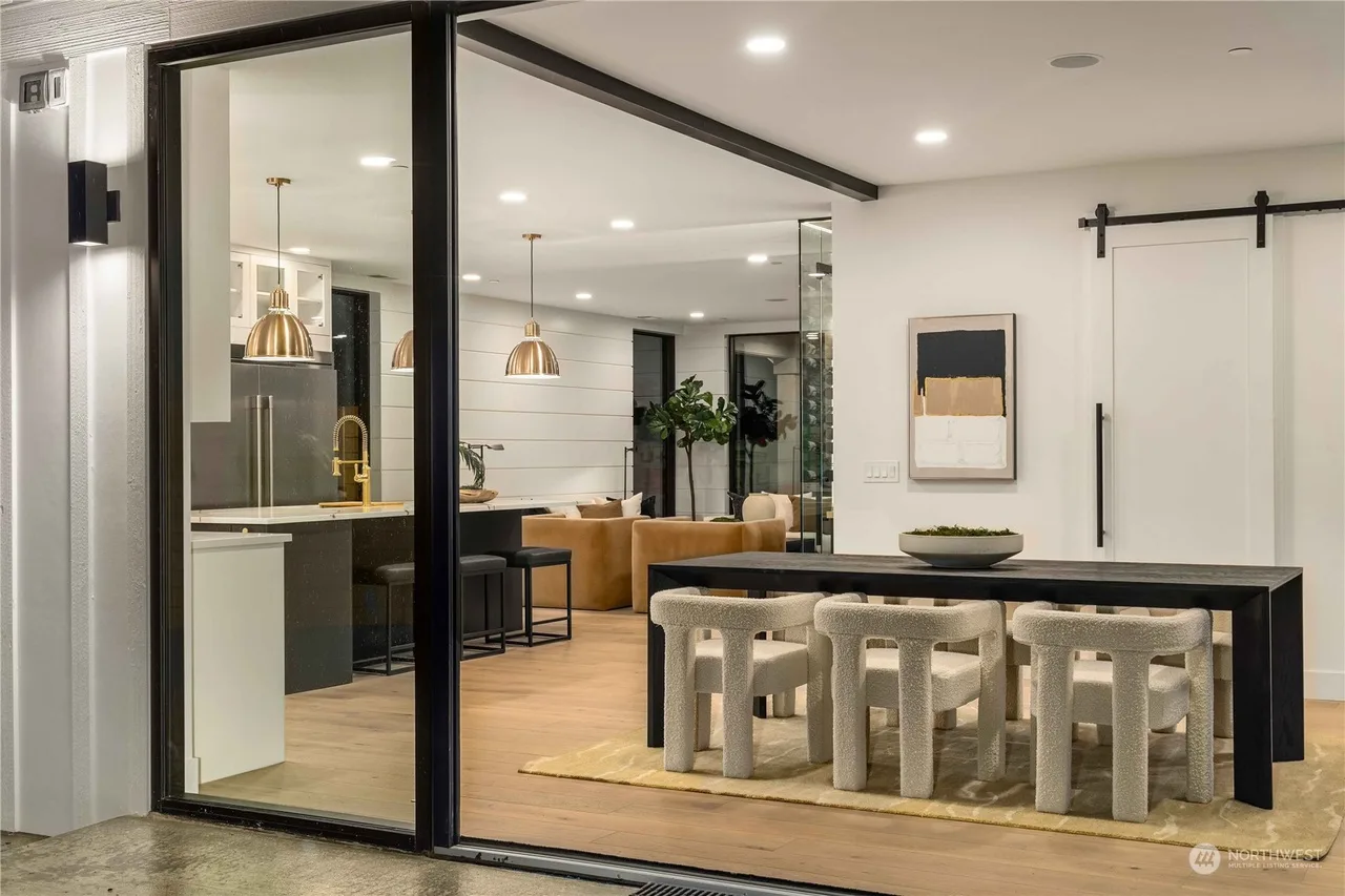 Black dining table and white chairs framed by the open sliding glass wall and a barn door on the main floor
