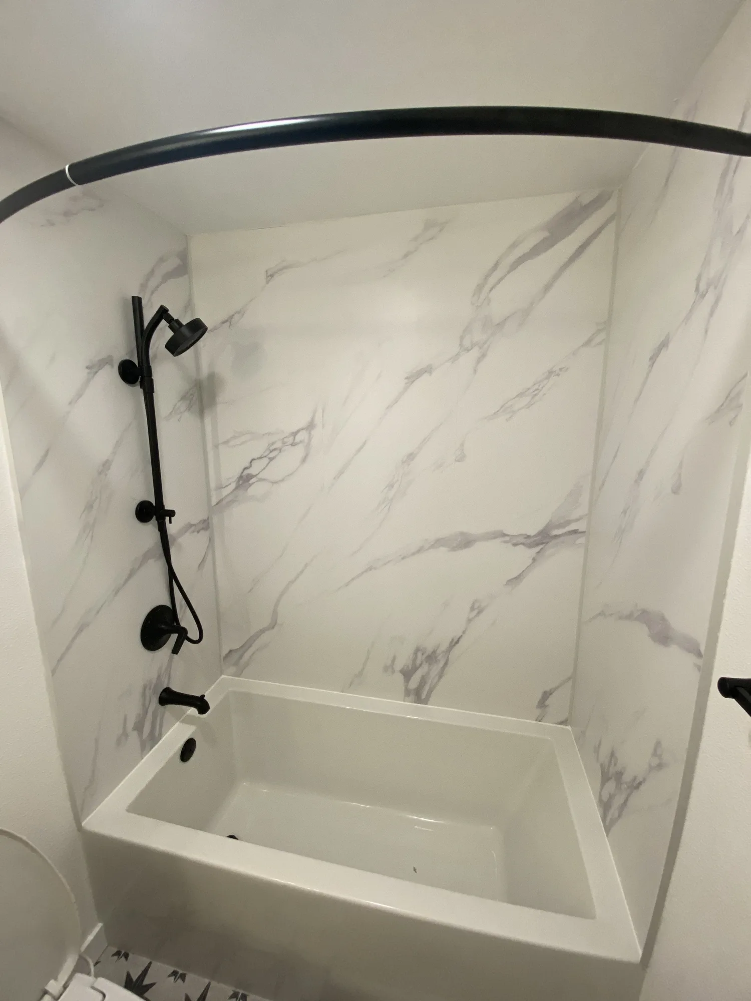 Soaker tub with a calacatta-look surround, matte-black rain shower, and curved black curtain rod