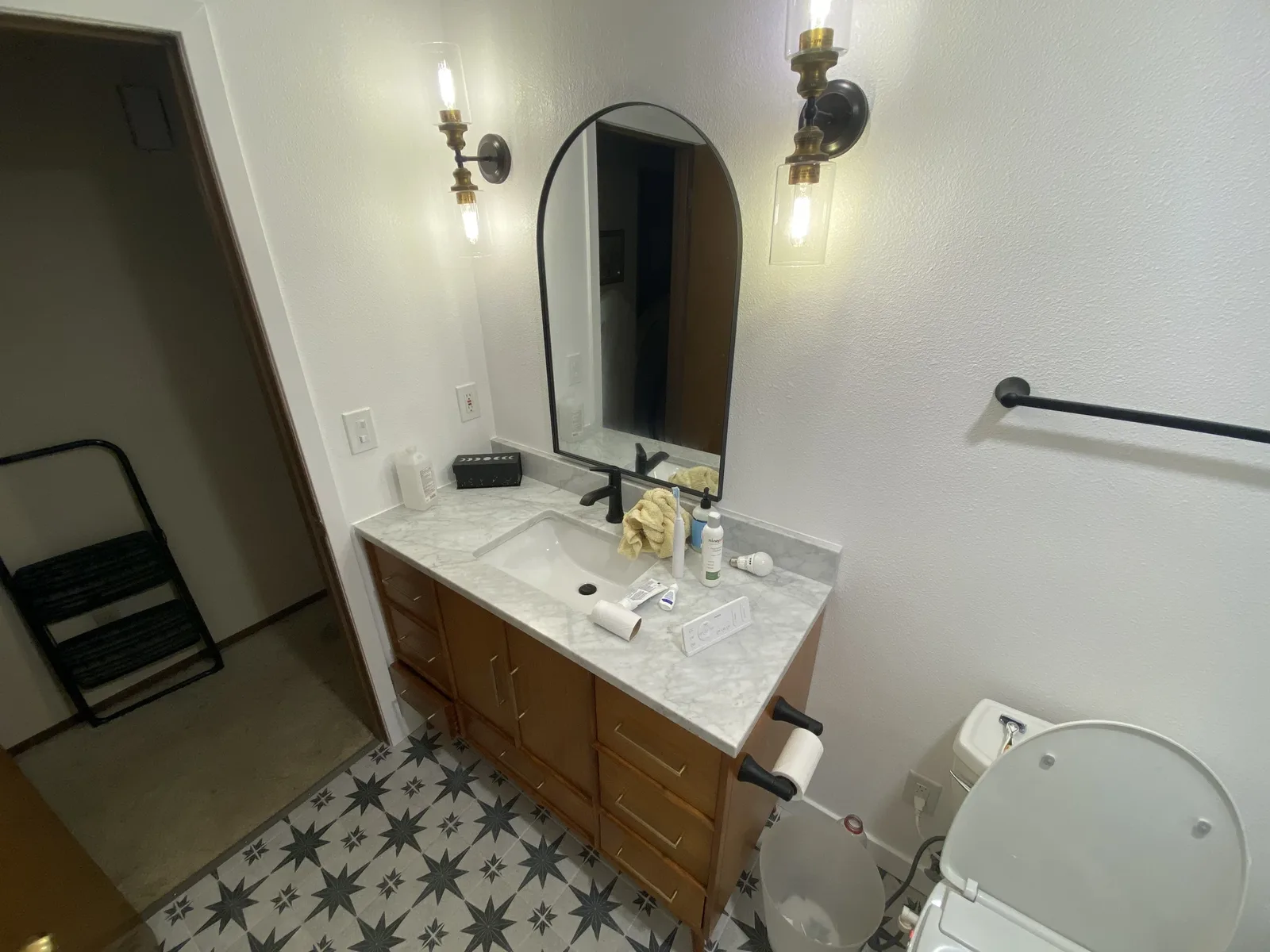 Wood vanity with marble top, arched black mirror, brass-and-glass sconces, and bidet smart toilet on star tile