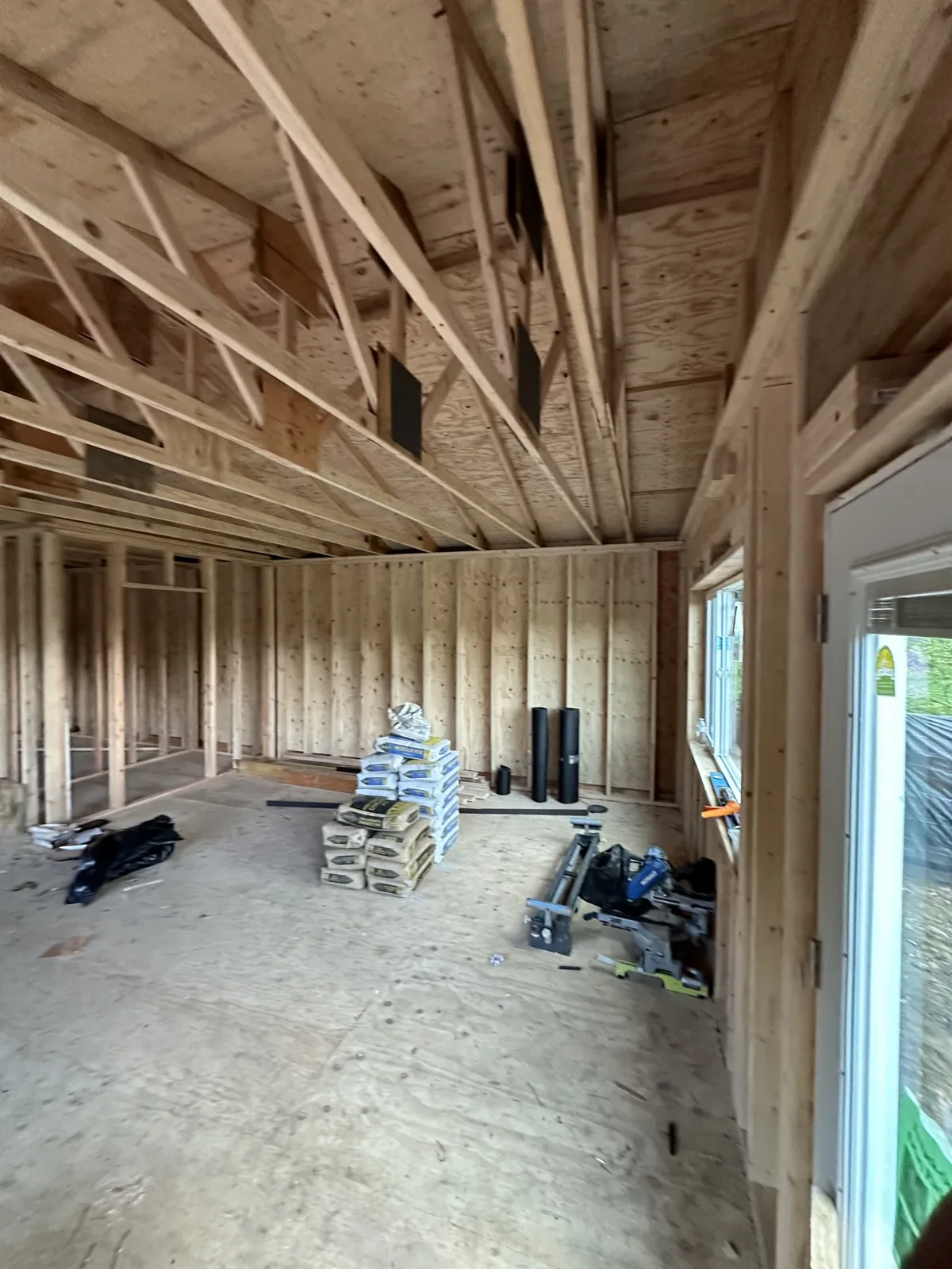 Wide interior framing view with trusses overhead and materials staged