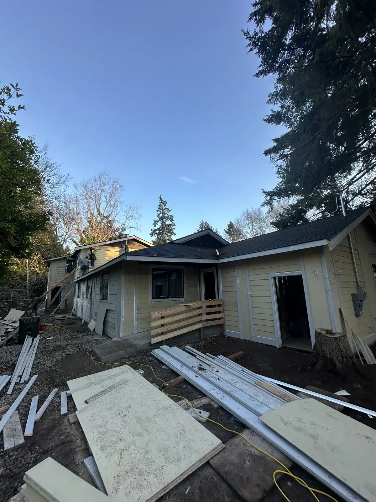 Primed siding with dark trim boards and materials staged along the house