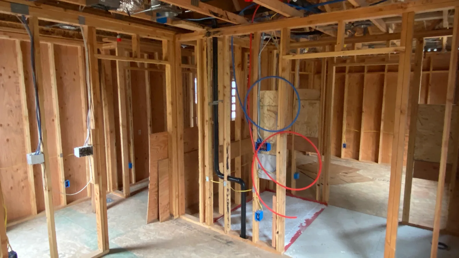 Red and blue PEX supply lines run through the framed bathroom wall