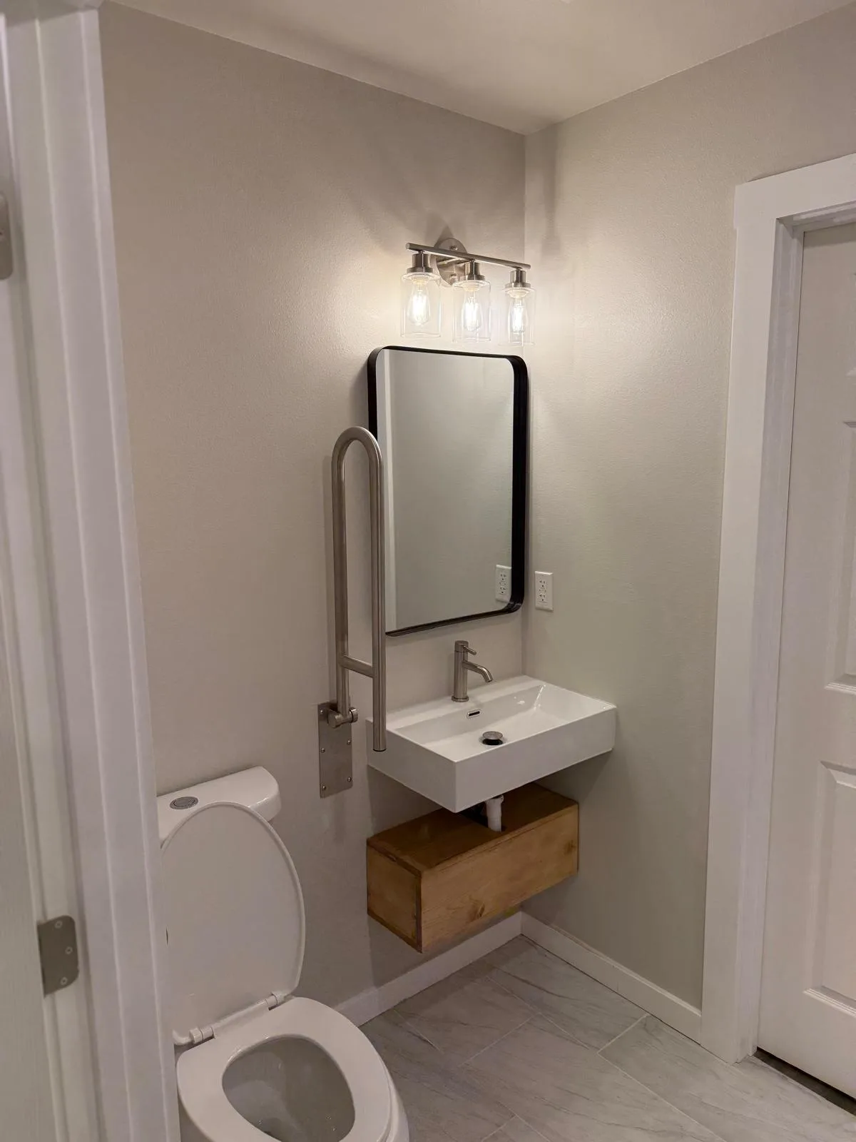 Bathroom with a wall-mount sink, black-frame mirror, sconce, and toilet