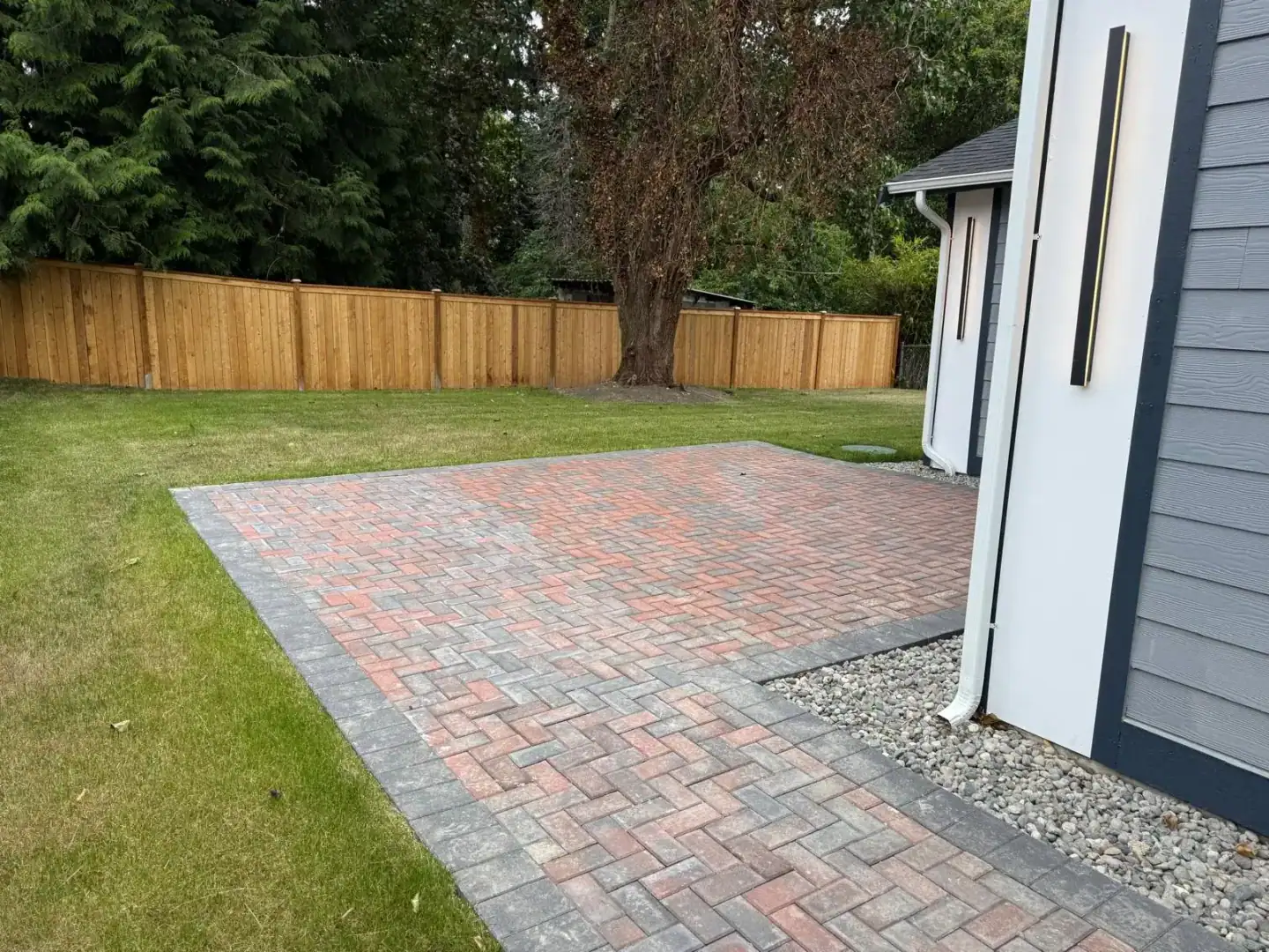 Herringbone paver patio beside the gray house with a new cedar fence