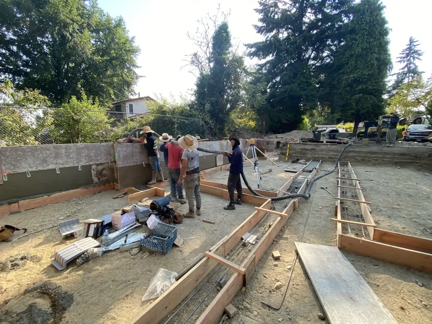 Crew setting footing and foundation wall forms with lumber staged on the pad