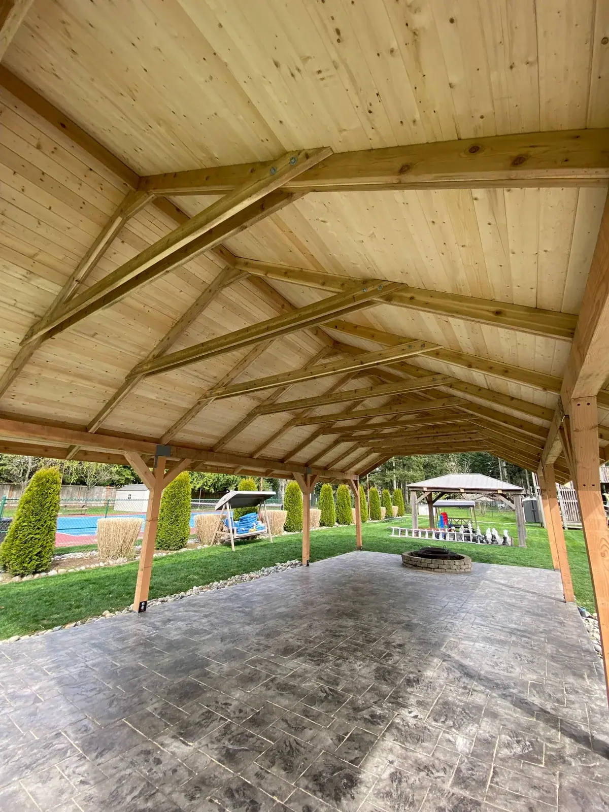 Underside of the pavilion roof with exposed cedar rafters and tongue-and-groove ceiling, pool beyond
