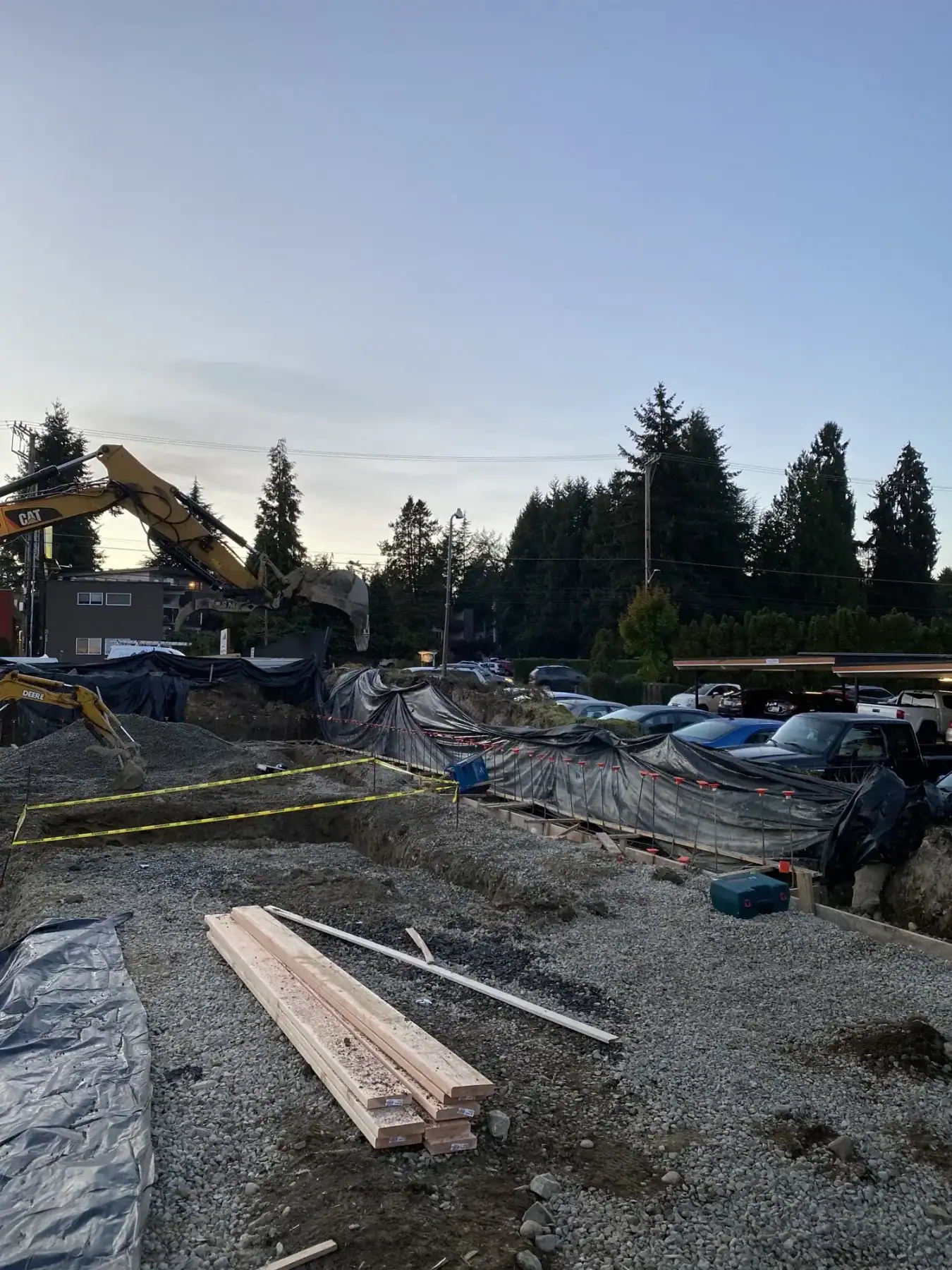 Excavator beside footing layout lumber on the compacted pad at dusk