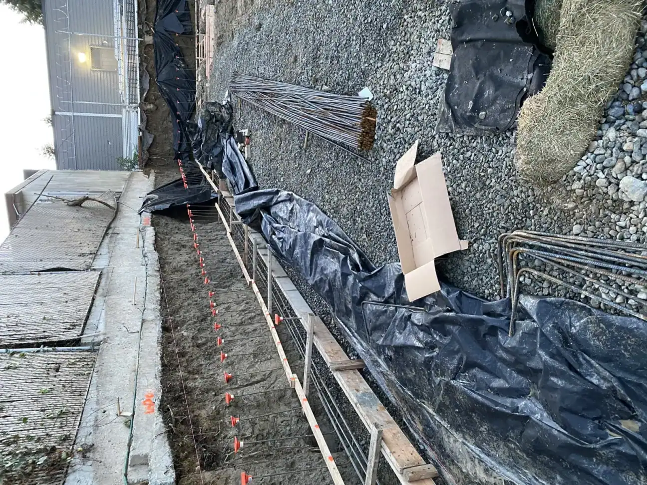 Footing trench along the wall with rebar, black membrane, drain, and a pink string line