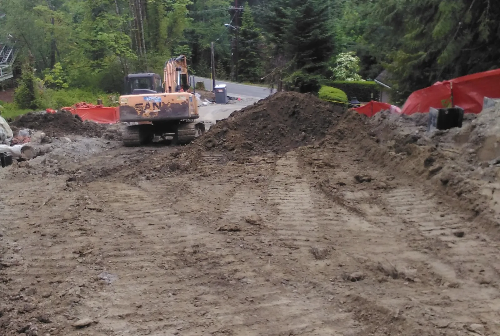 Graded dirt hillside with an excavator and orange construction fence