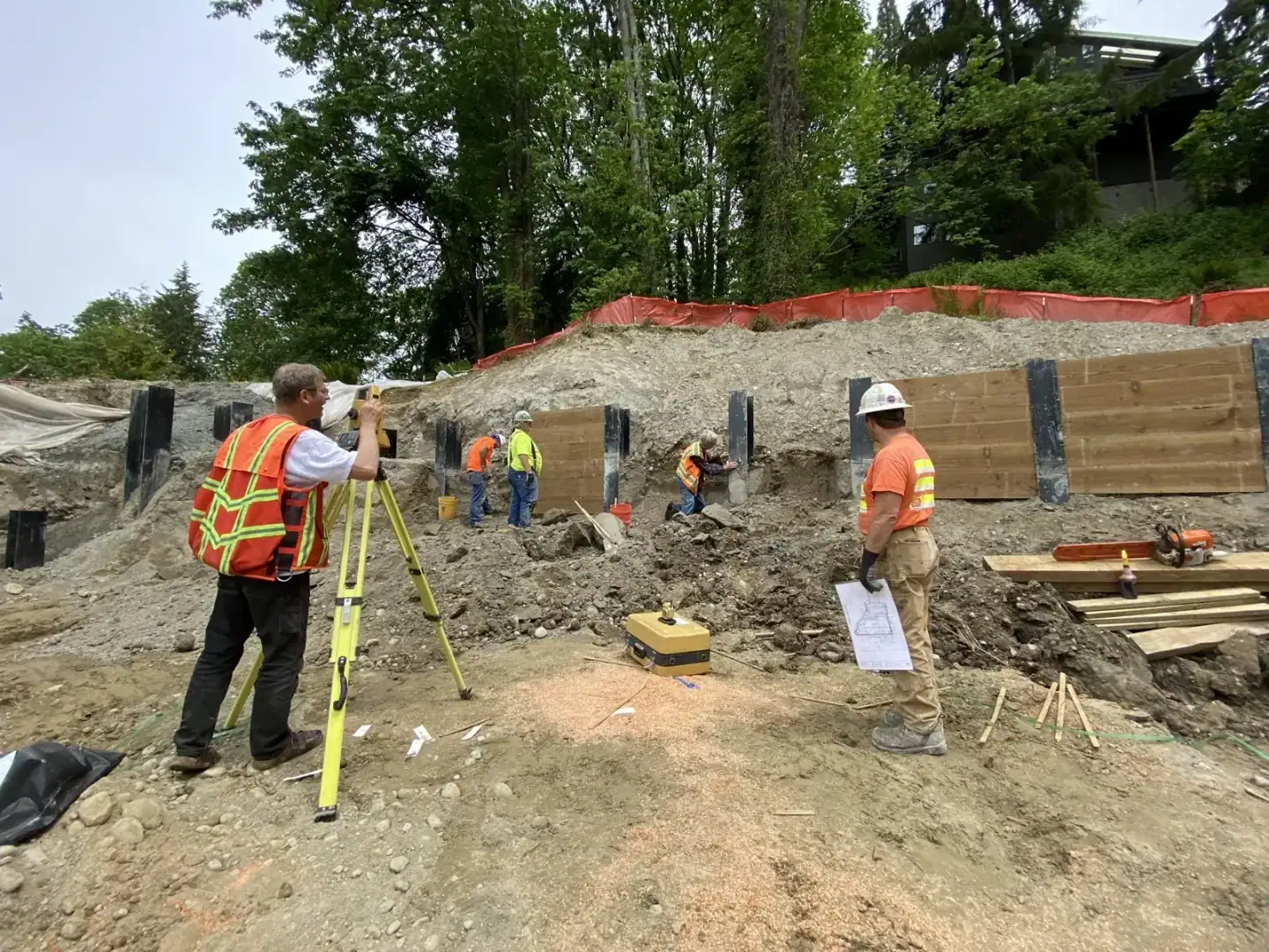 Survey crew with a total station setting the soldier-pile wall line as steel piles stand ready