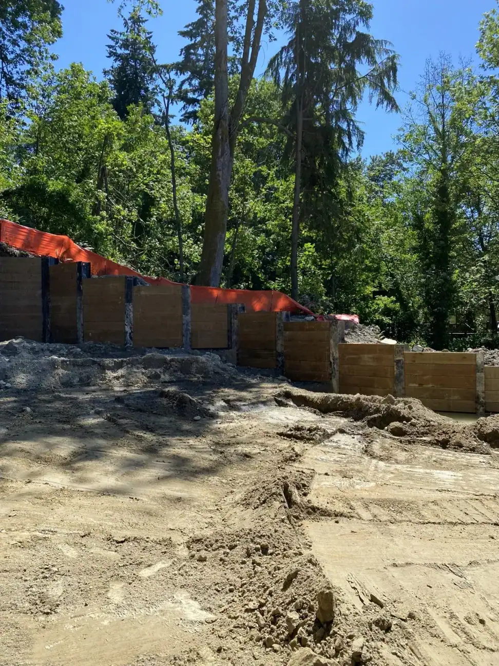 Soldier-pile wall with timber lagging under construction against the wooded slope