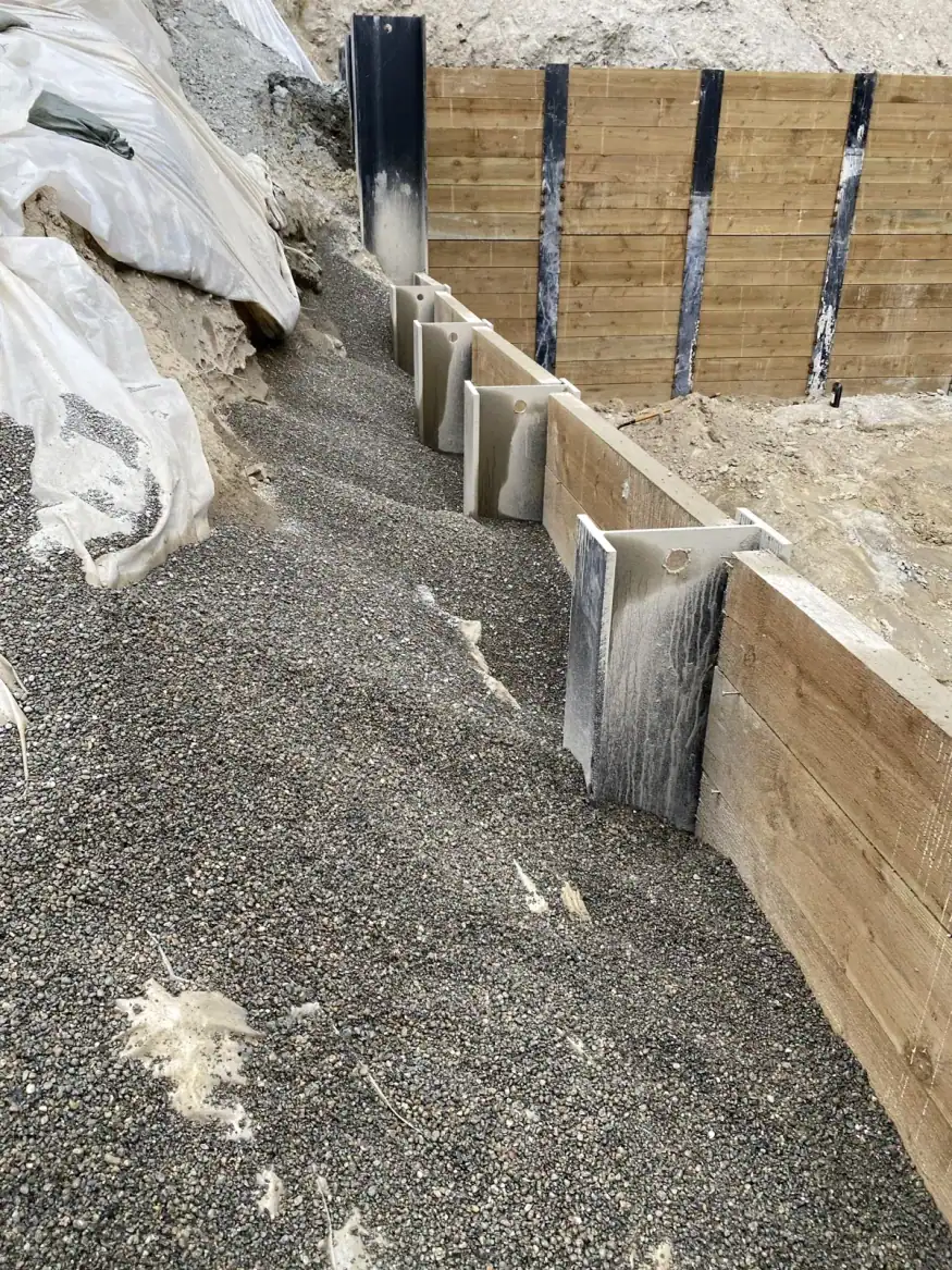 Close-up of a steel H-pile with treated-timber lagging and drain rock backfill