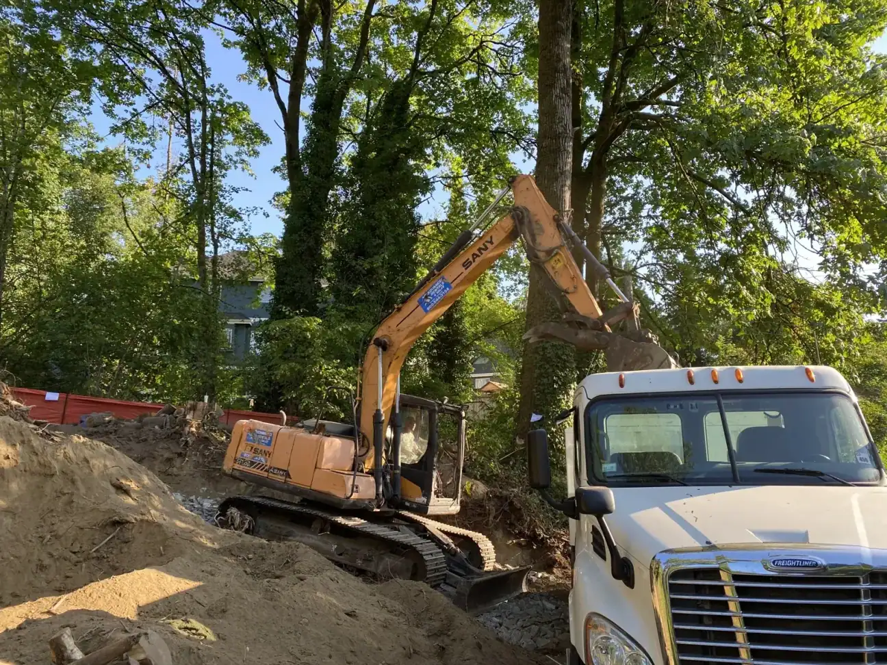 Excavator digging beside a white dump truck during cut-to-grade