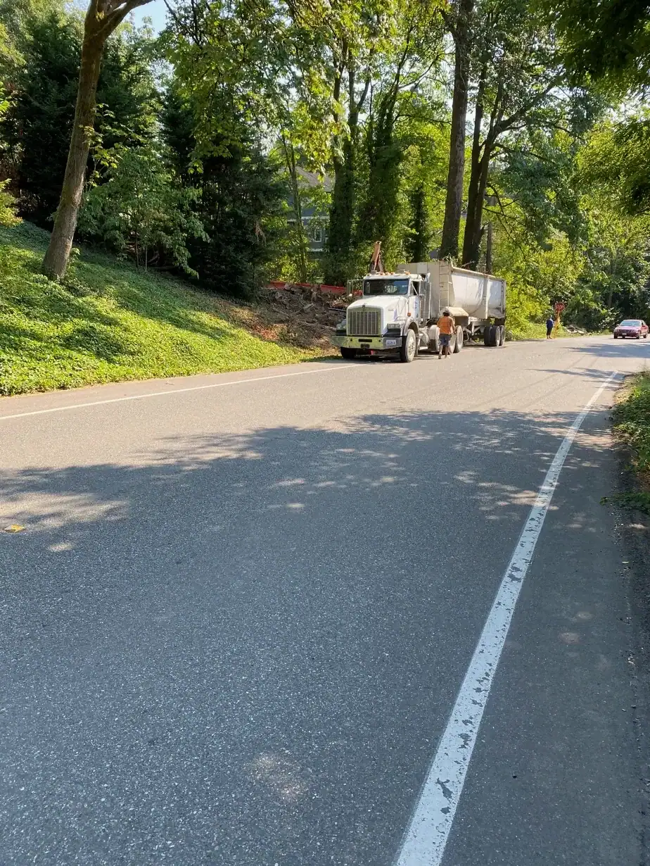 Dump truck parked on the shoulder of the neighborhood road below the site