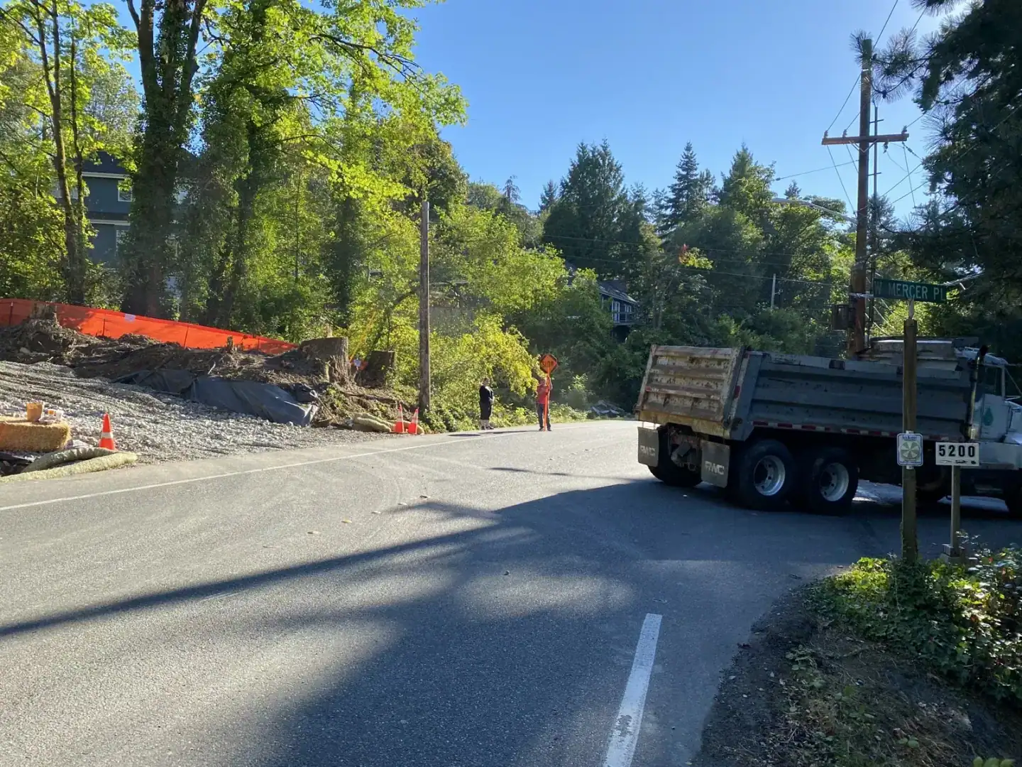 Dump truck on the roadway beside the orange-fenced site with traffic control in place