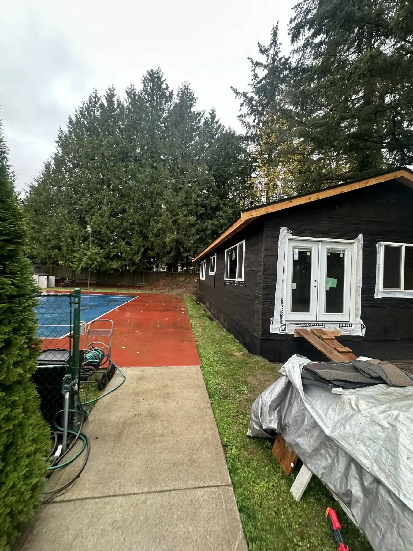 Black-sided DADU with white windows beside the property's red sport court
