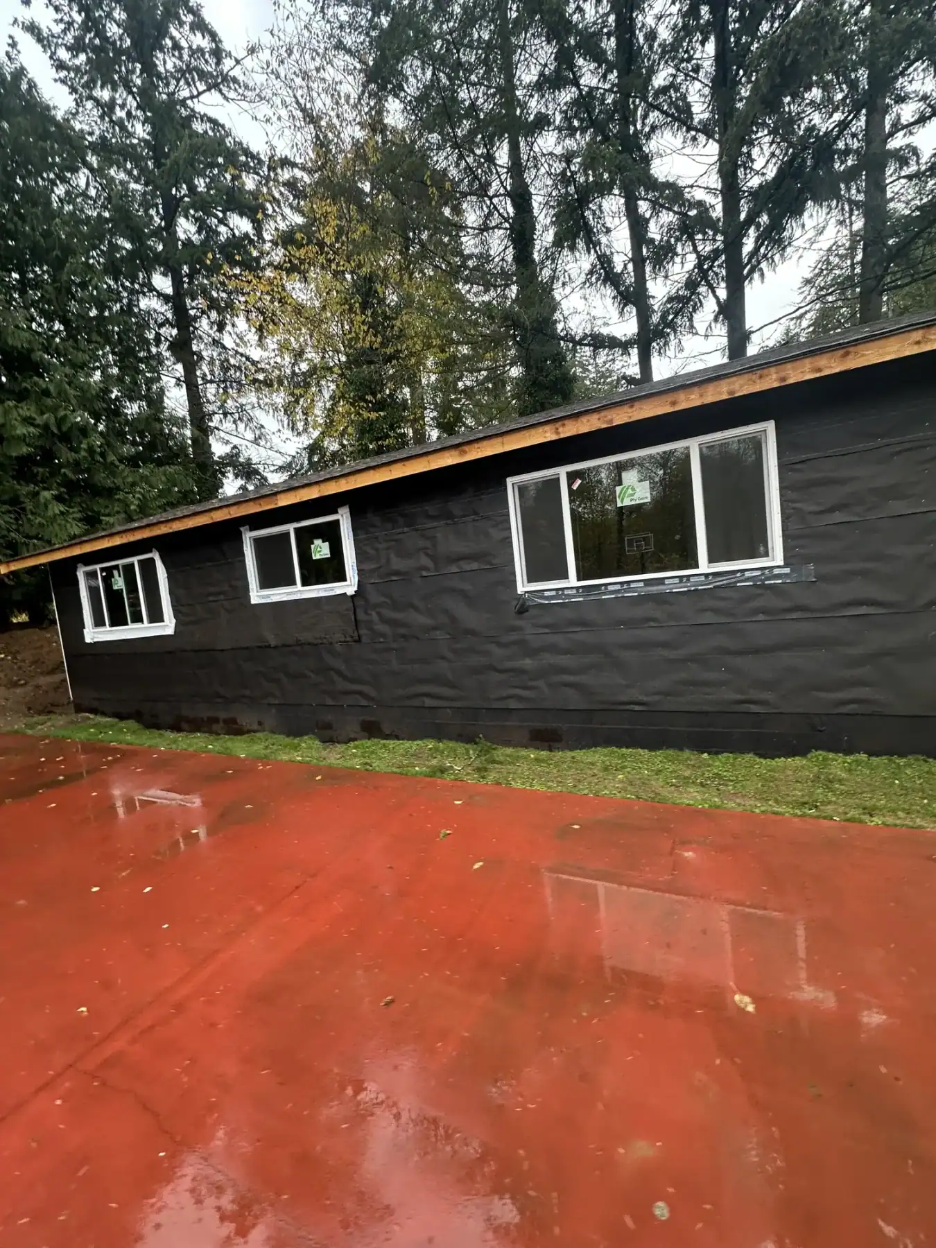 Black exterior of the detached ADU with wide windows facing the red court surface