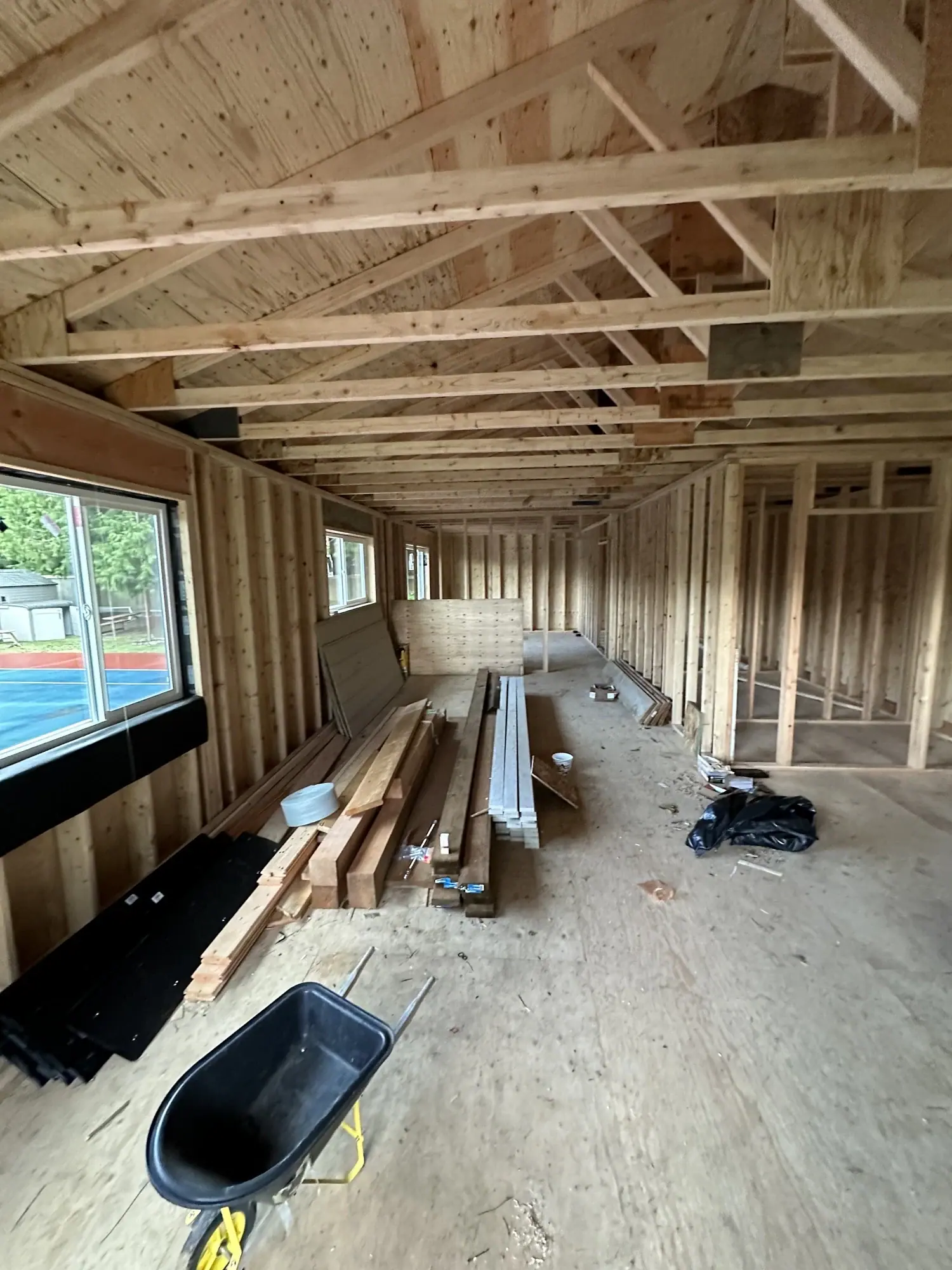 Framed DADU interior with trusses, a wheelbarrow, and window openings