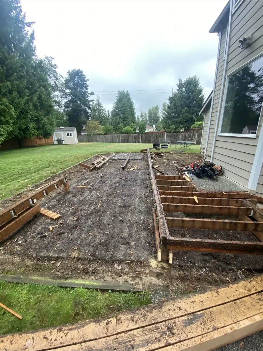 Deck footprint cleared to bare soil with old joists and the first form boards in place