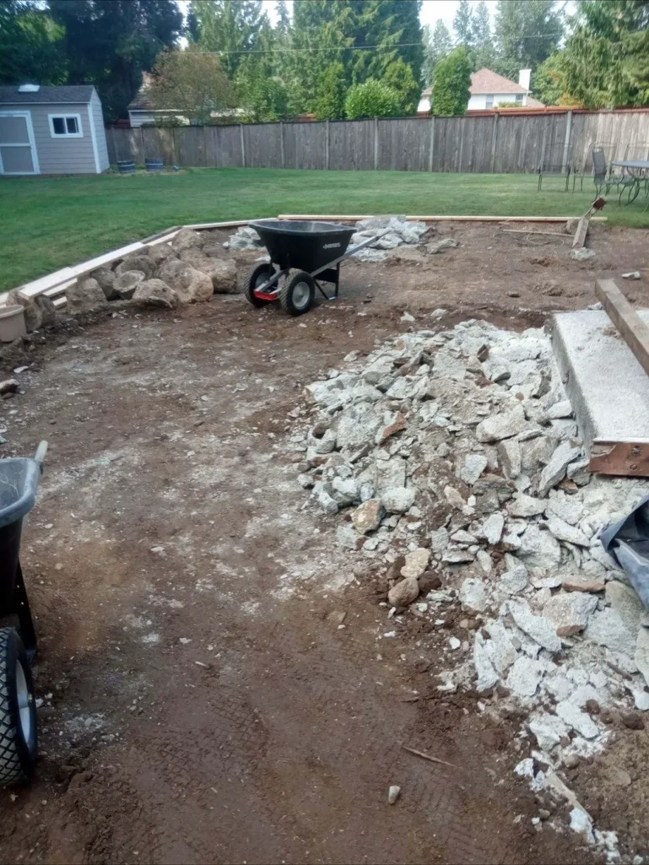 Pile of broken concrete and a wheelbarrow beside the cleared patio area