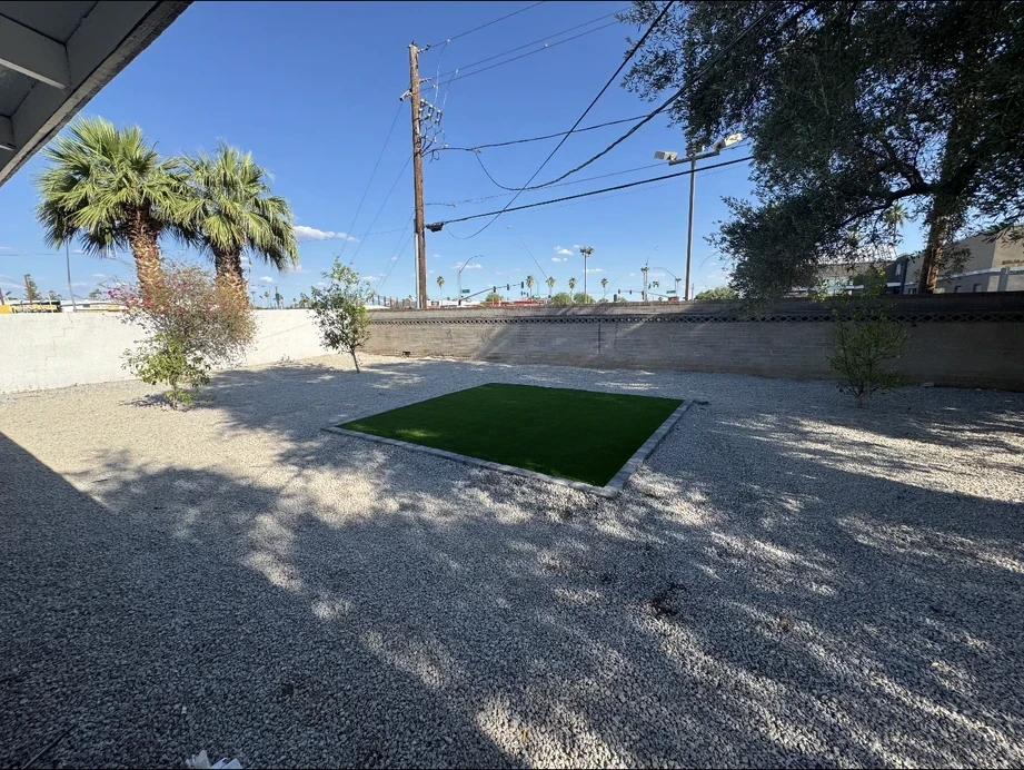 Finished desert yard with decorative rock, an artificial-turf inset, palms, and the block wall