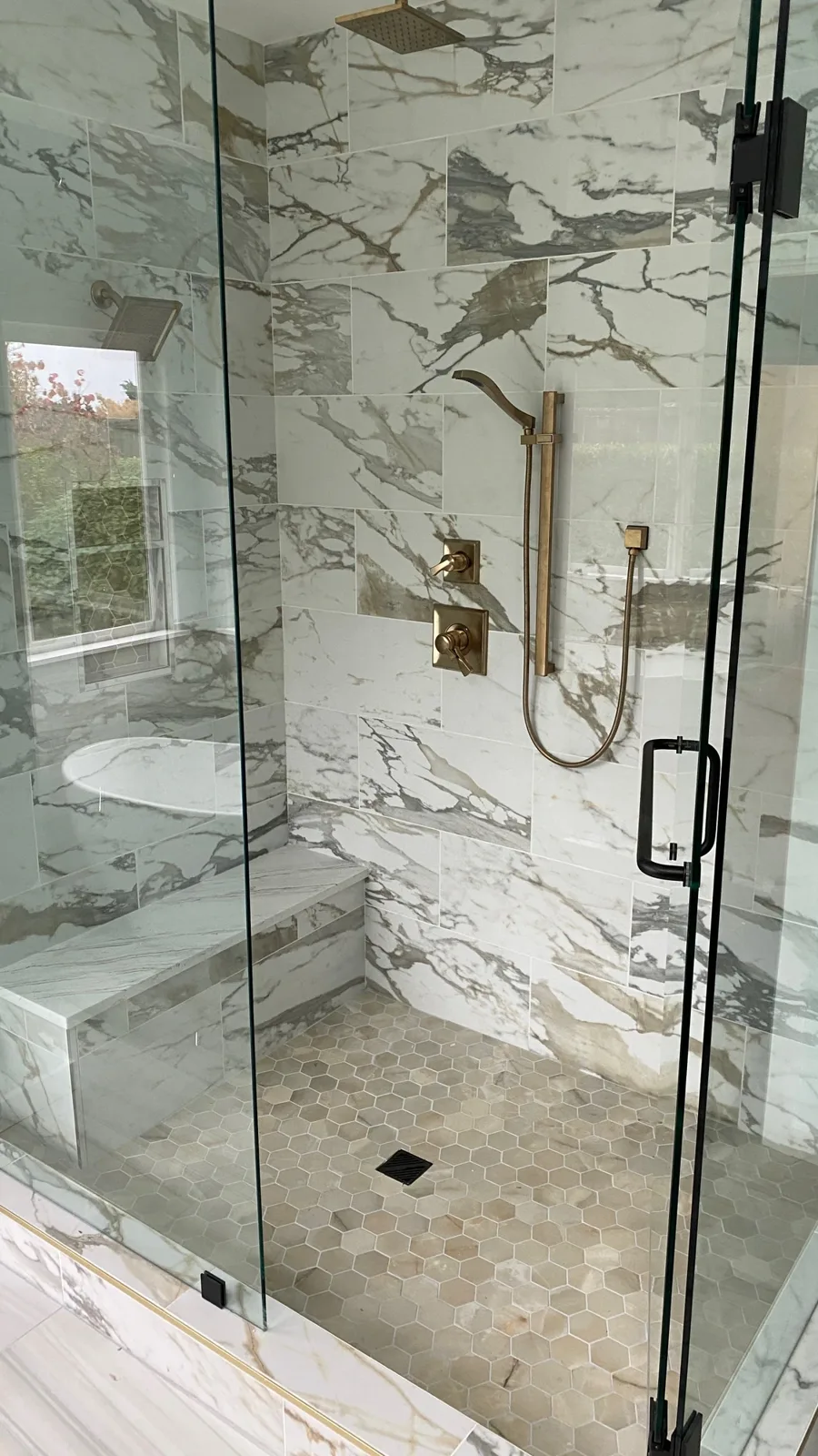Calacatta-look shower with a brushed-gold handheld shower and frameless glass