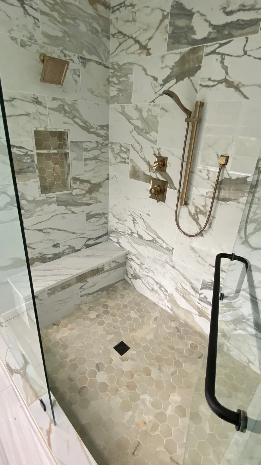 Shower bench and tile niche behind a glass door with a black handle