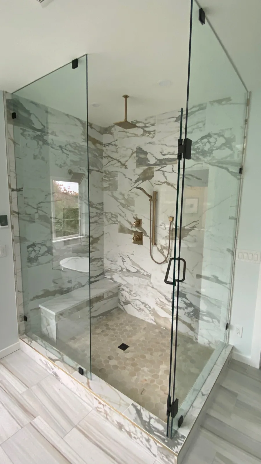 Frameless glass corner shower with a bench and hex-mosaic pan