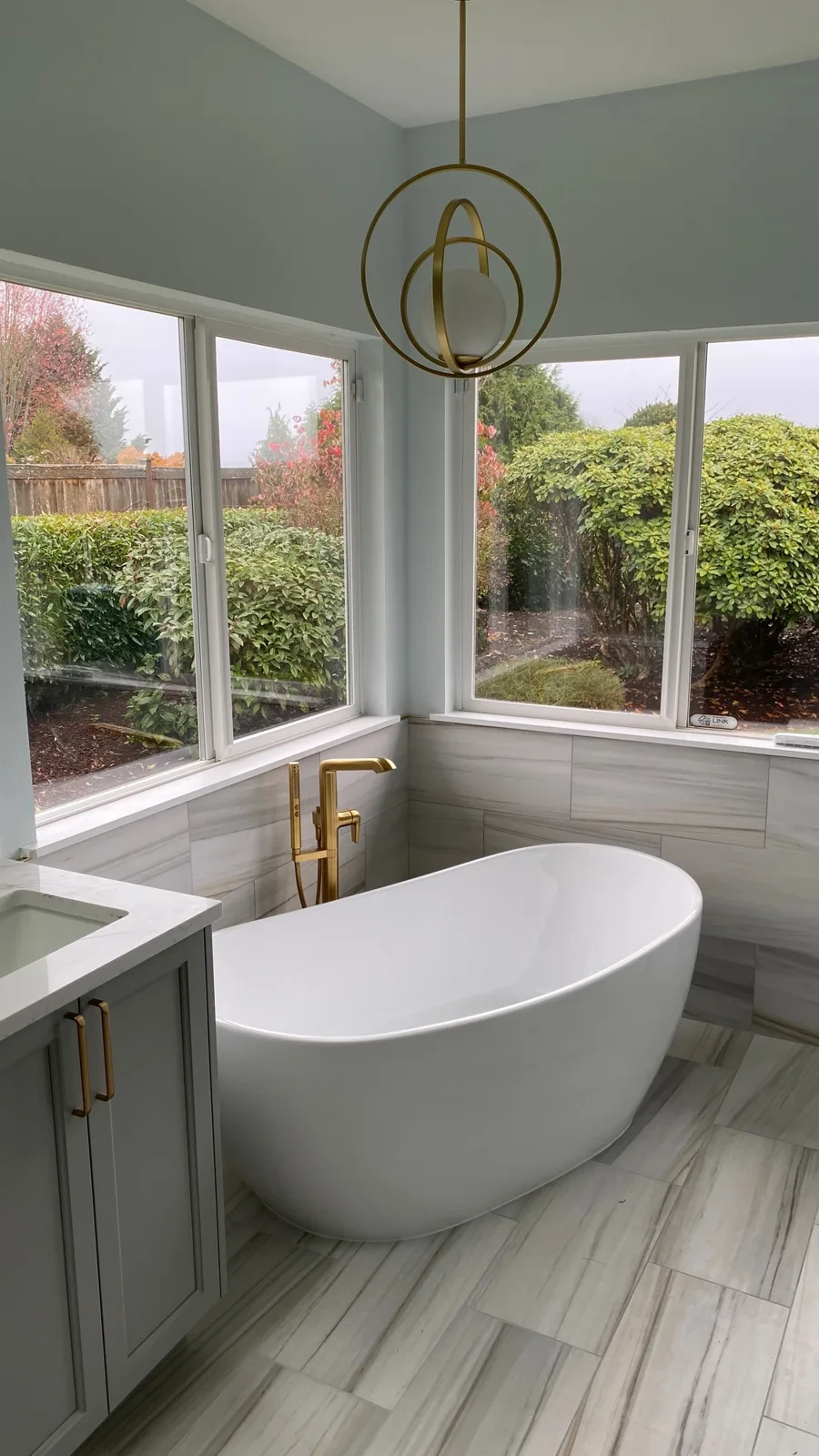 Freestanding tub in the window bay with a brushed-gold filler and brass pendant